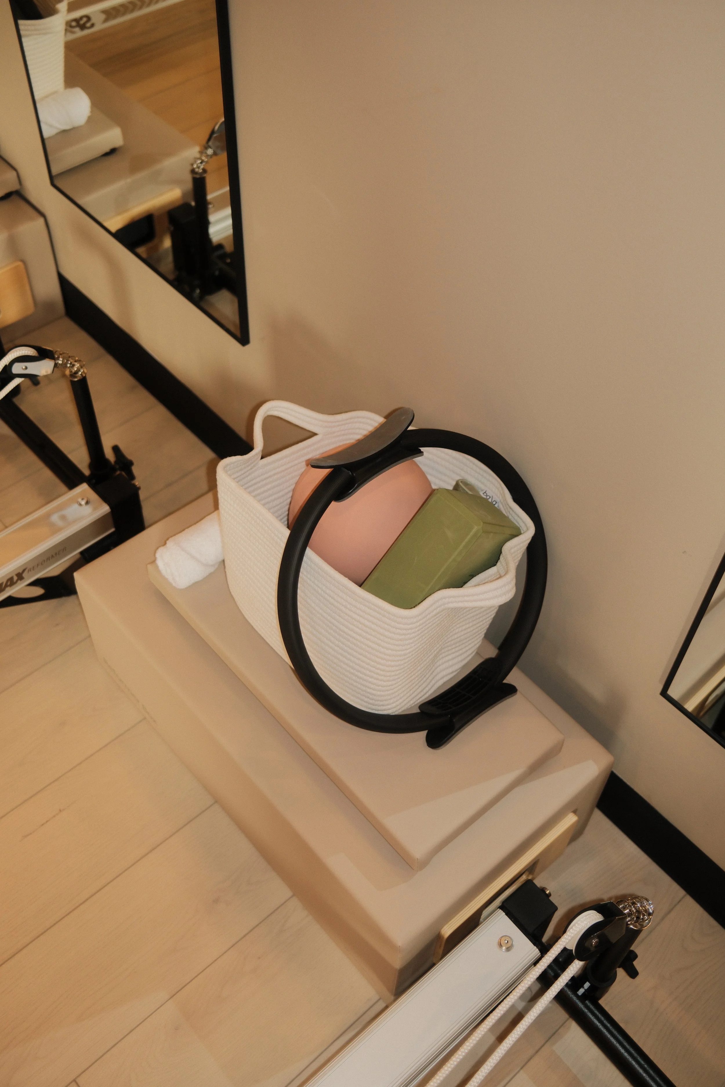 A white handbag on a beige surface contains a pink round object and a green rectangular item, placed next to a mirror and a fitness machine.