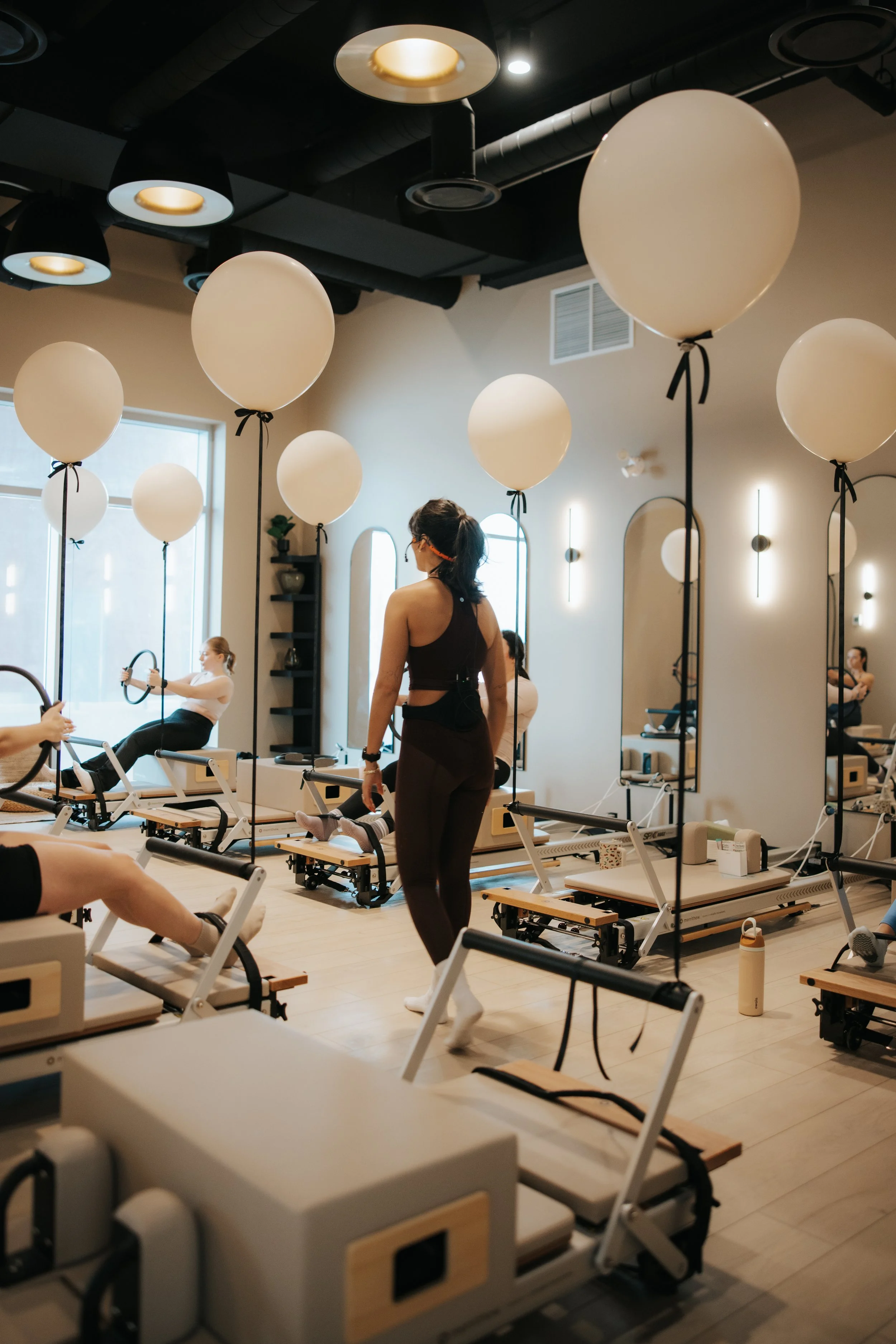 Pilates class in a studio decorated with white balloons tied to Pilates reformer machines and large windows allowing natural light.
