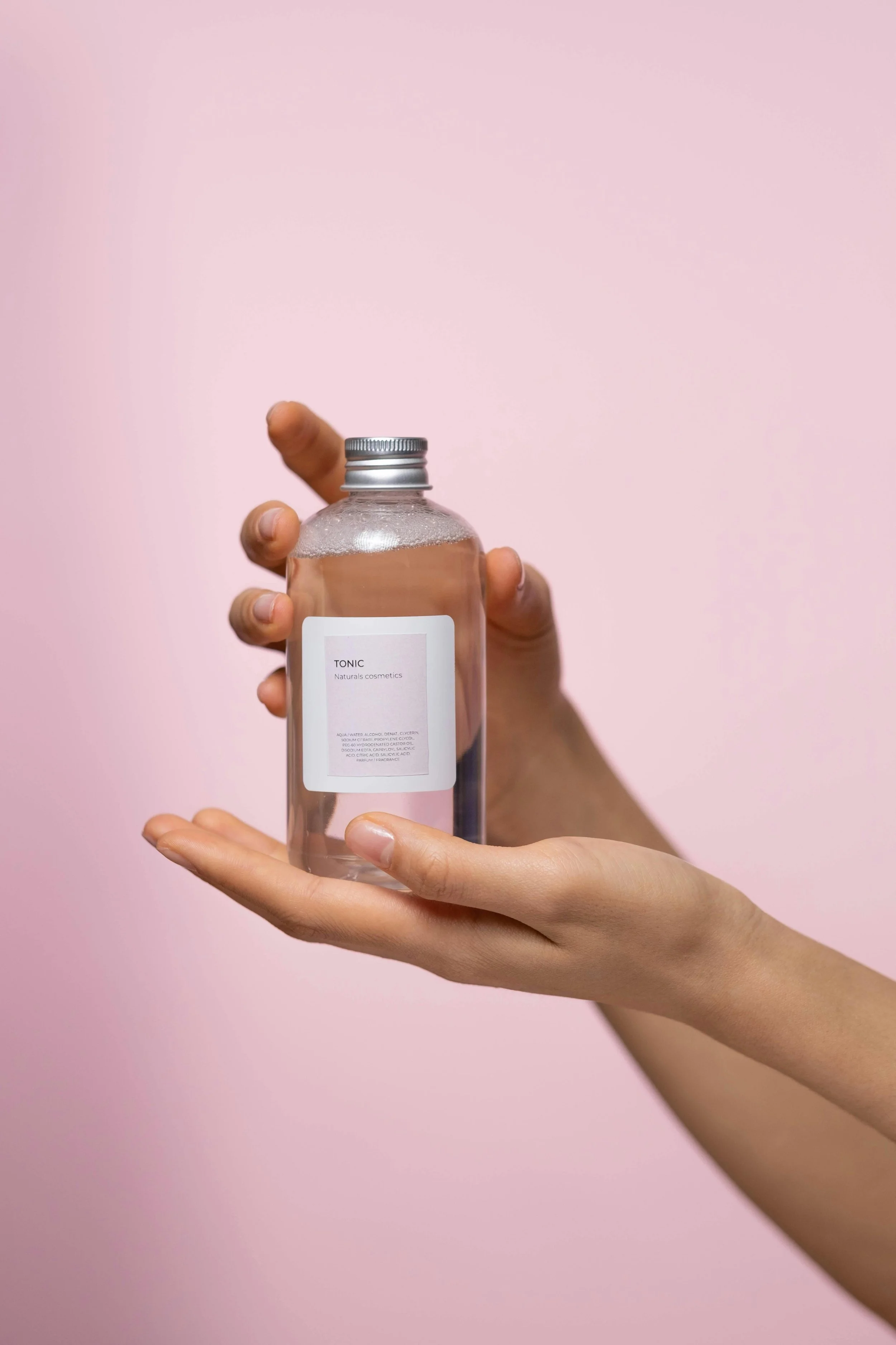 Skincare bottle being held in a woman's hand with a pastel pink background