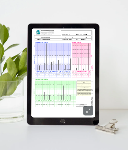 A tablet displaying a medical or laboratory report with color-coded charts in blue, pink, and green, placed on a white desk with a glass bowl of green leaves on the left and metal clips on the right.