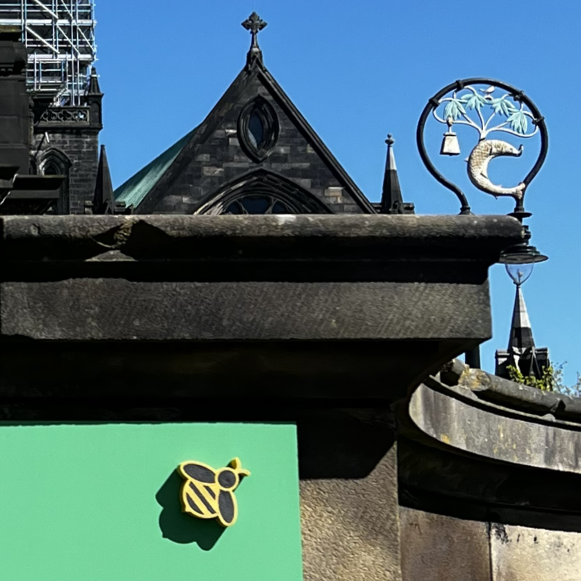 yellow and black jesmonite bee on stone wall with glasgow coat of arms and cathedral in background