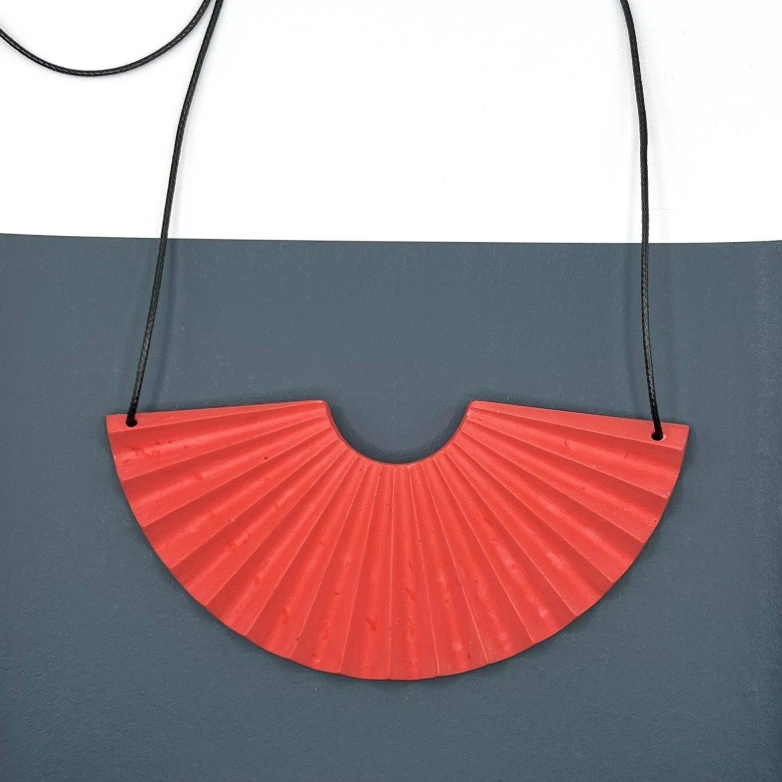 red jesmonite fan shaped statement necklace with adjustable black cord designed by studio mariscat on grey background