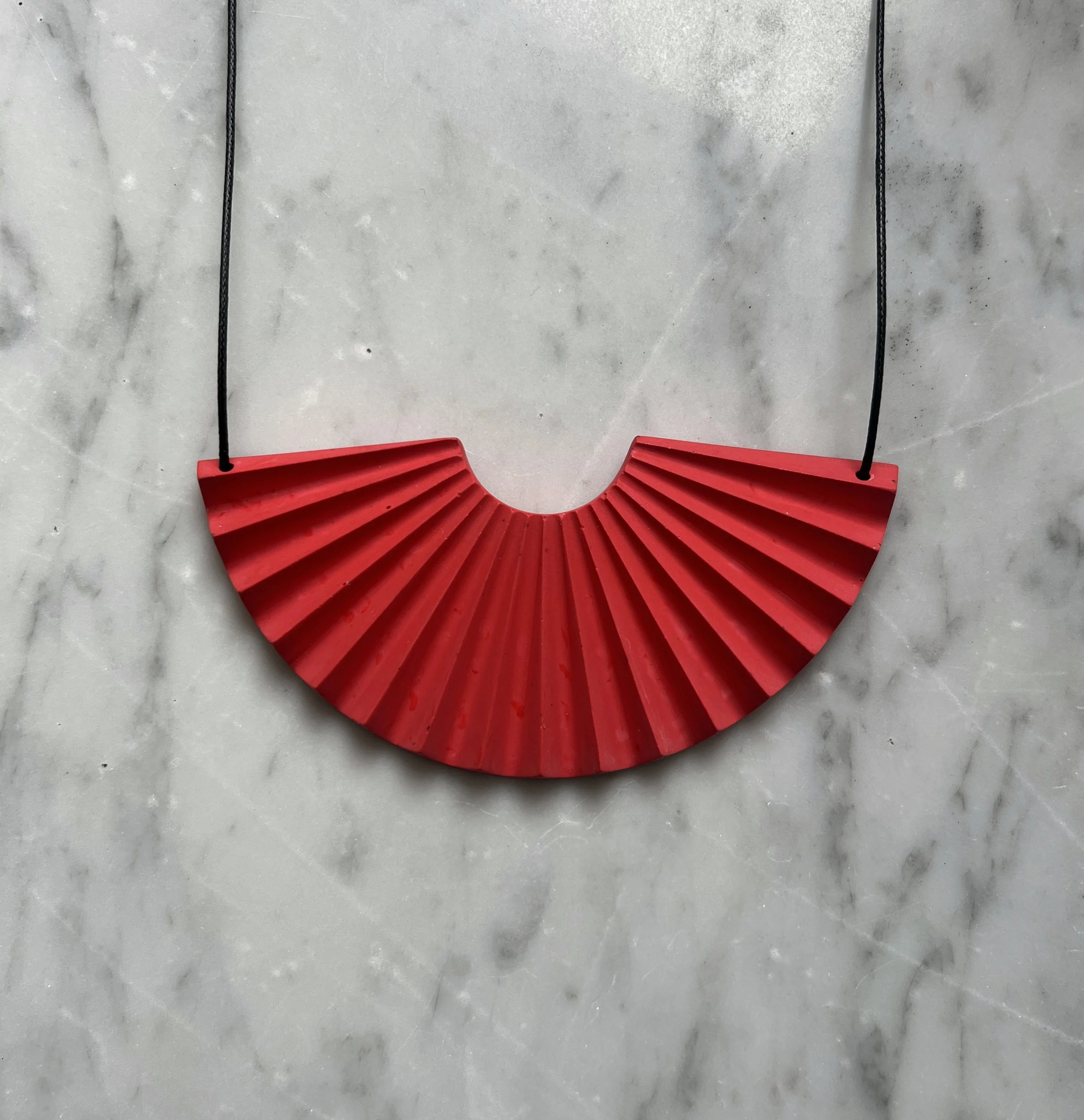 red jesmonite fan shaped statement necklace with adjustable black cord designed by studio mariscat marble background
