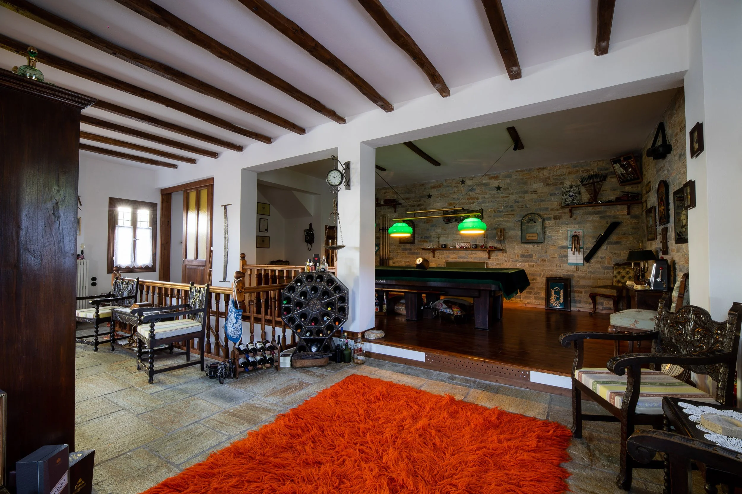 Living room with stone and brick wall, pool table with green lamp overhead, vintage chairs, orange shag rug, and decorative wall art.