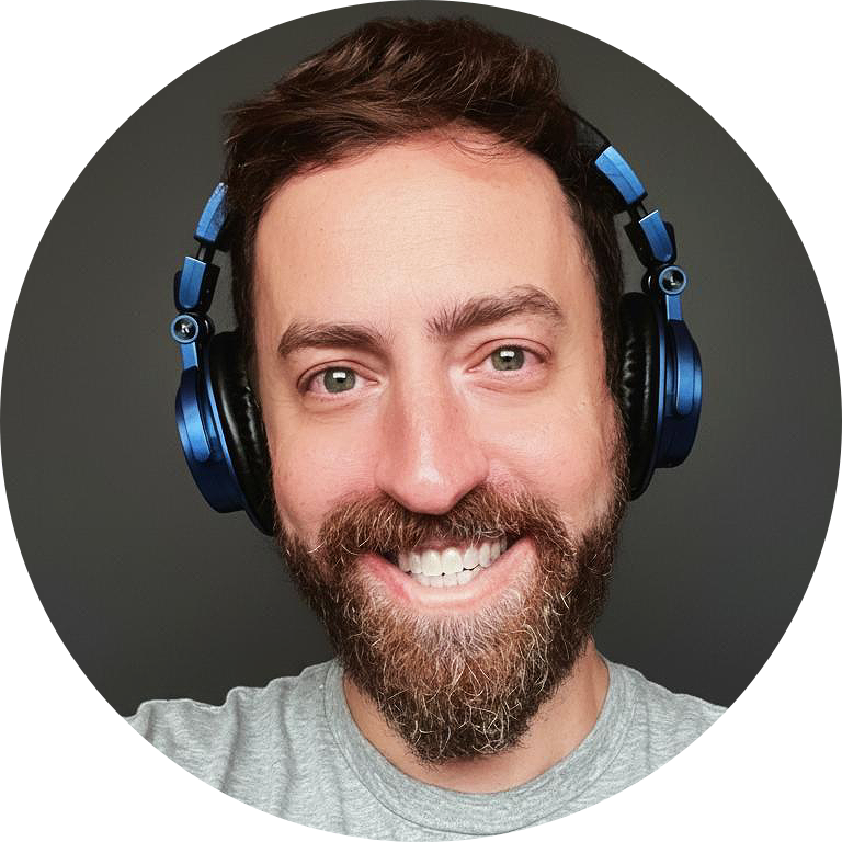 A smiling man with a beard and light-colored eyes wearing blue headphones against a dark background.