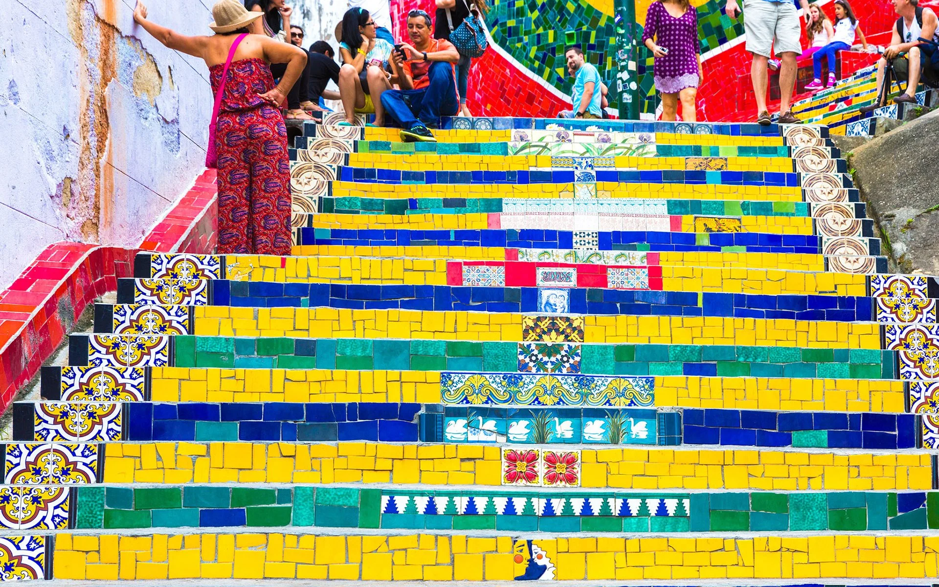 View of the colorful Selarón Stairway in Rio de Janeiro, covered in vibrant ceramic tiles from around the world, leading uphill through a bustling neighborhood.