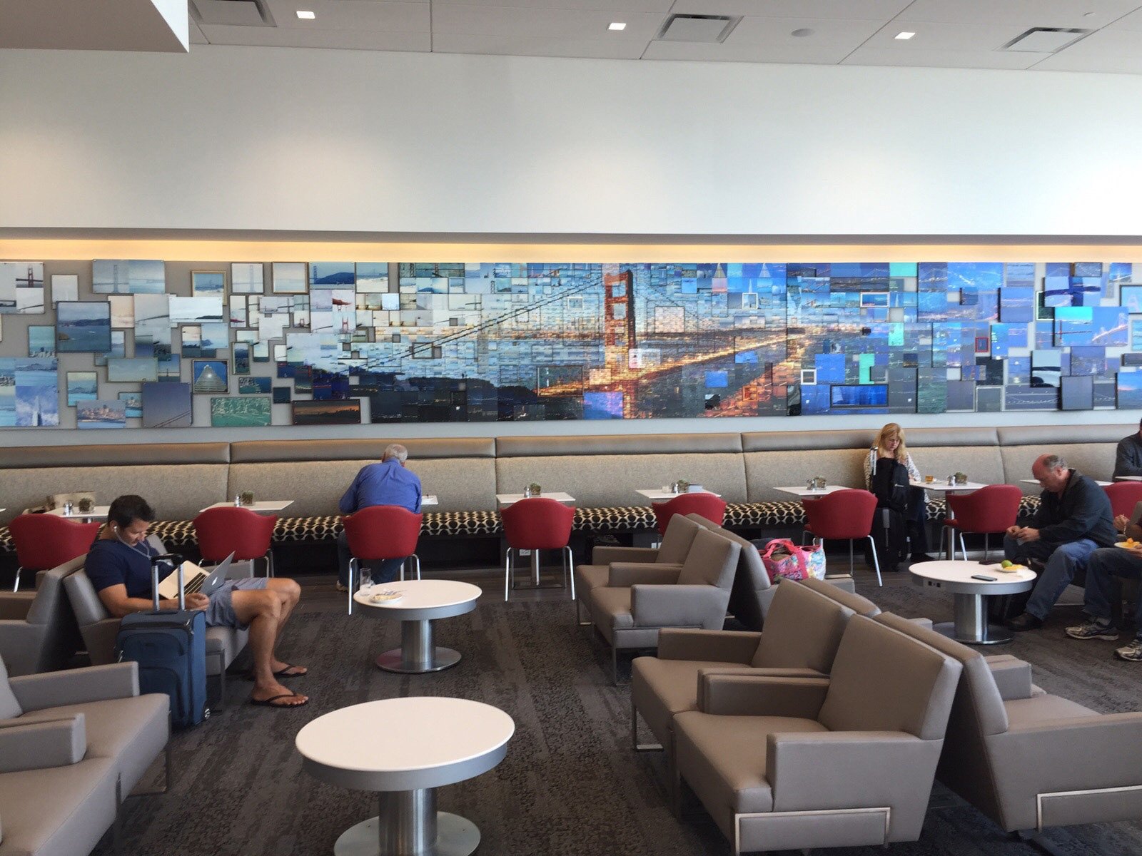  Travellers relaxing in the Delta Sky Club at San Francisco under a wide mosaic mural of the Golden Gate Bridge 