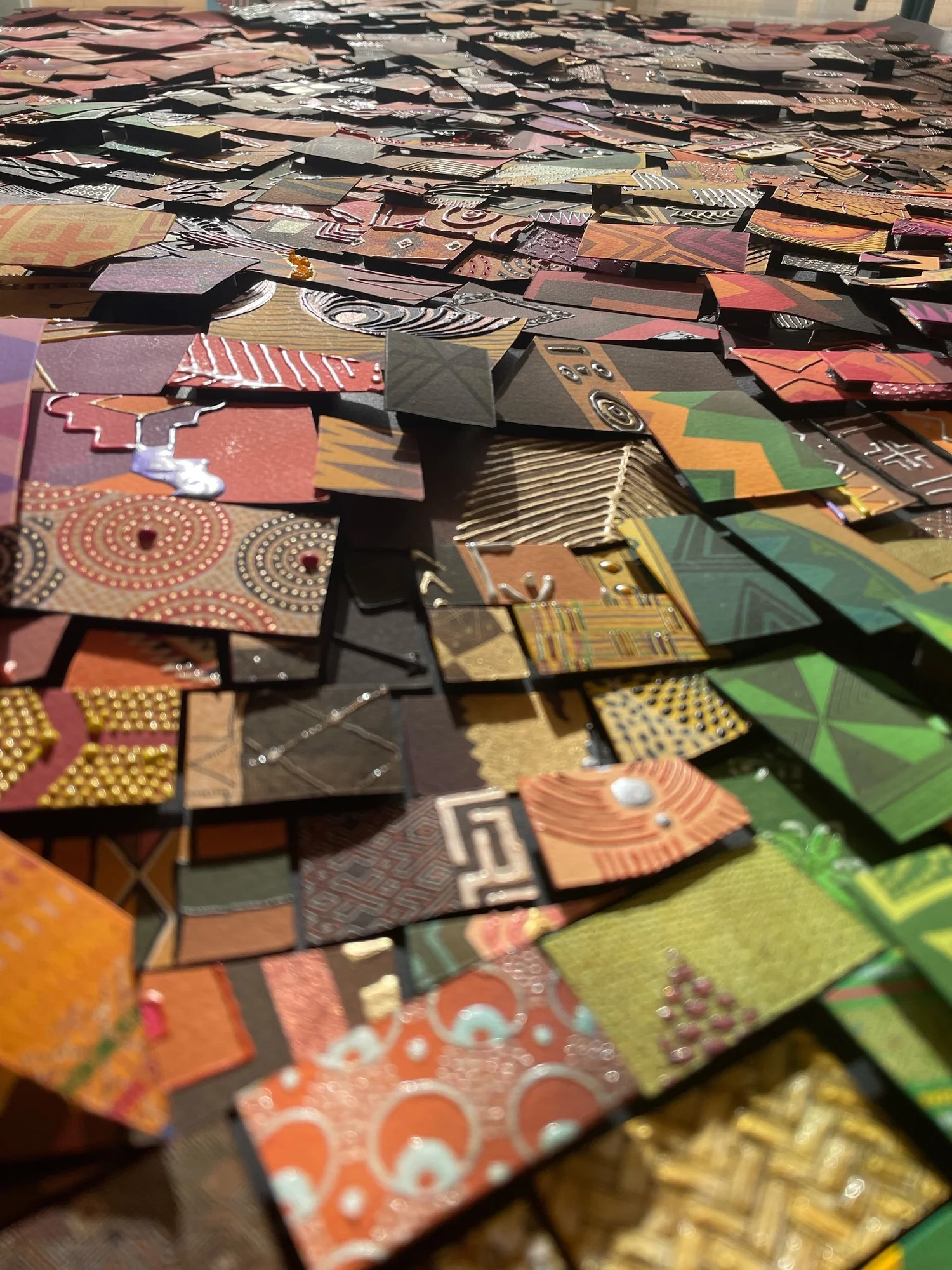 Close-up of a heap of small patterned paper tiles in orange, green, gold and red, ready for mosaic work