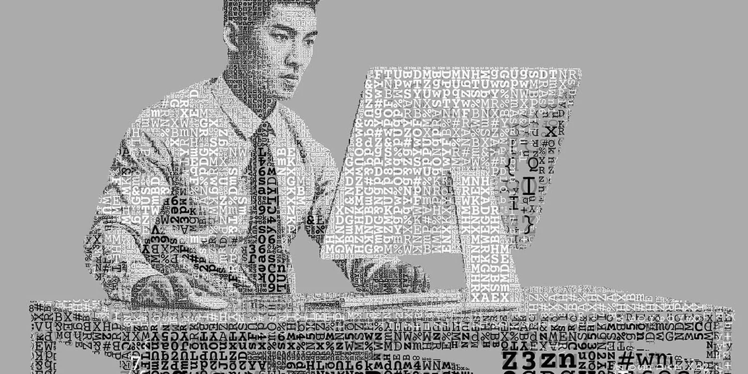 A grayscale multilayered ascii art typographic portrait of a man sitting at a desk, composed entirely of random letters, numbers, and symbols. The intricate design uses the density and arrangement of text to form the contours of his face, clothing, and posture, creating a striking visual effect against a plain gray background.