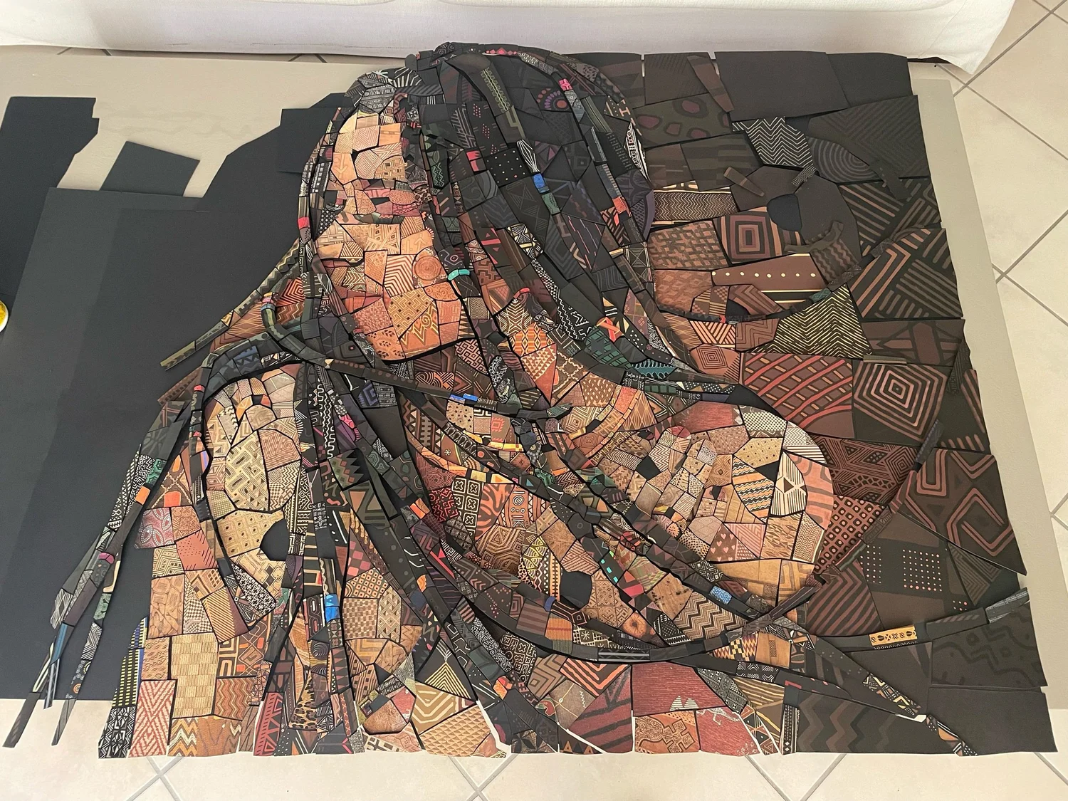 Large handmade paper mosaic of a woman with long braids lying on a floor, made from dark brown and copper patterned tiles