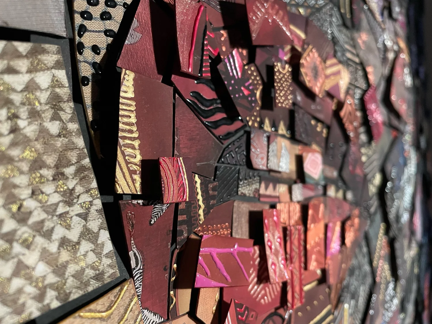 Side-angle close-up of layered paper mosaic tiles in red, pink and gold with shiny patterned surfaces and raised edges