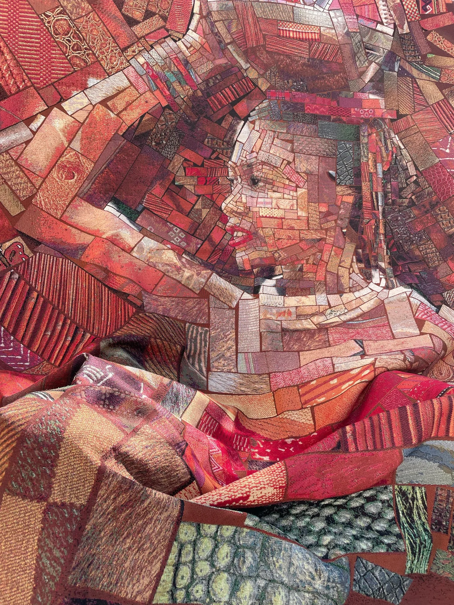 Close-up of a draped woven red mosaic fabric showing a face in profile made from small brick-like patterned tiles