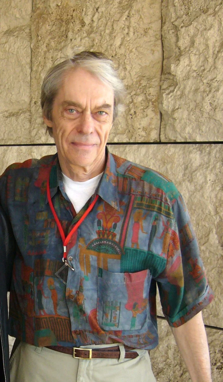 Ken Knowlton, grey-haired, in a patterned short-sleeved shirt, standing against a stone wall