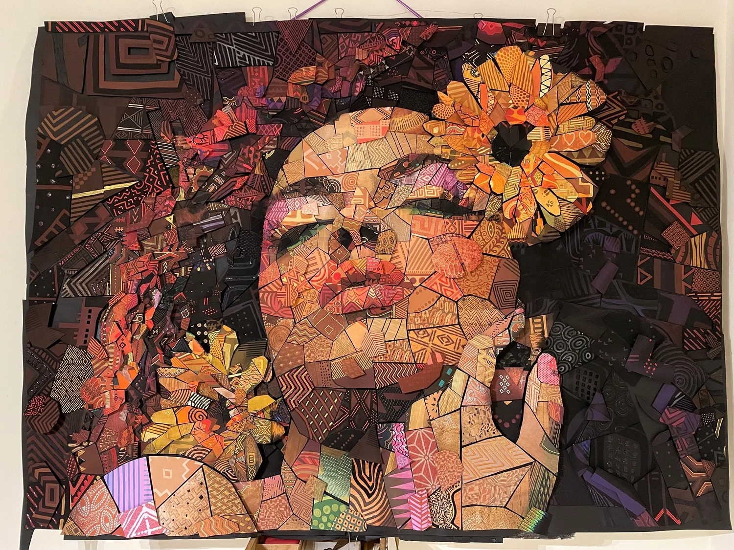 Handmade paper mosaic of a woman's face with a large orange flower in her hair, built from patterned cut tiles