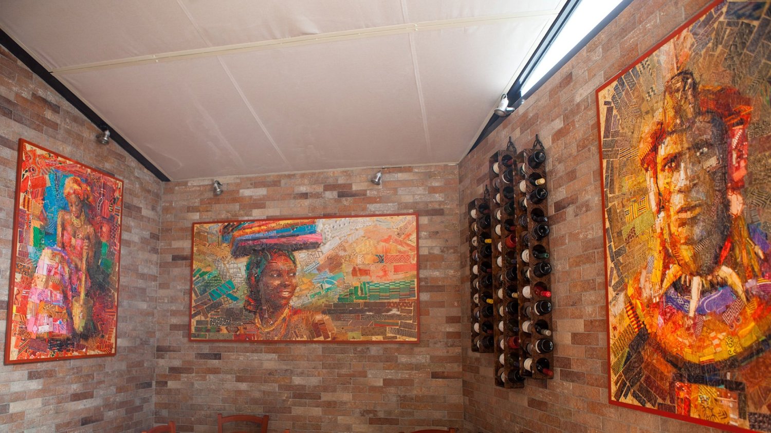 Restaurant interior with brick walls, wine racks and large framed mosaic portraits of African people hanging on the walls