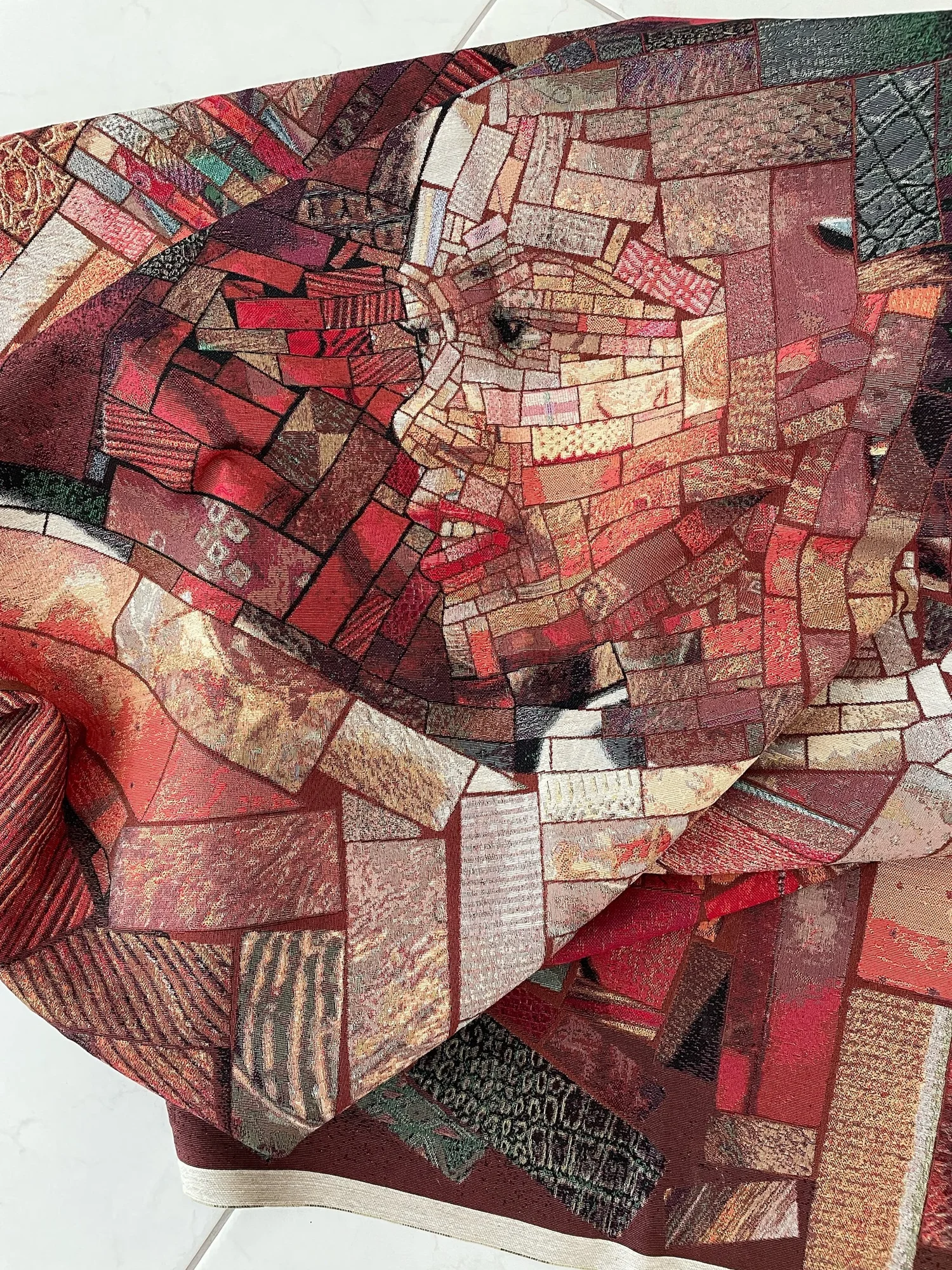 Close-up of a jacquard woven red mosaic fabric, folded, showing a face made from small patterned brick-like tile pieces