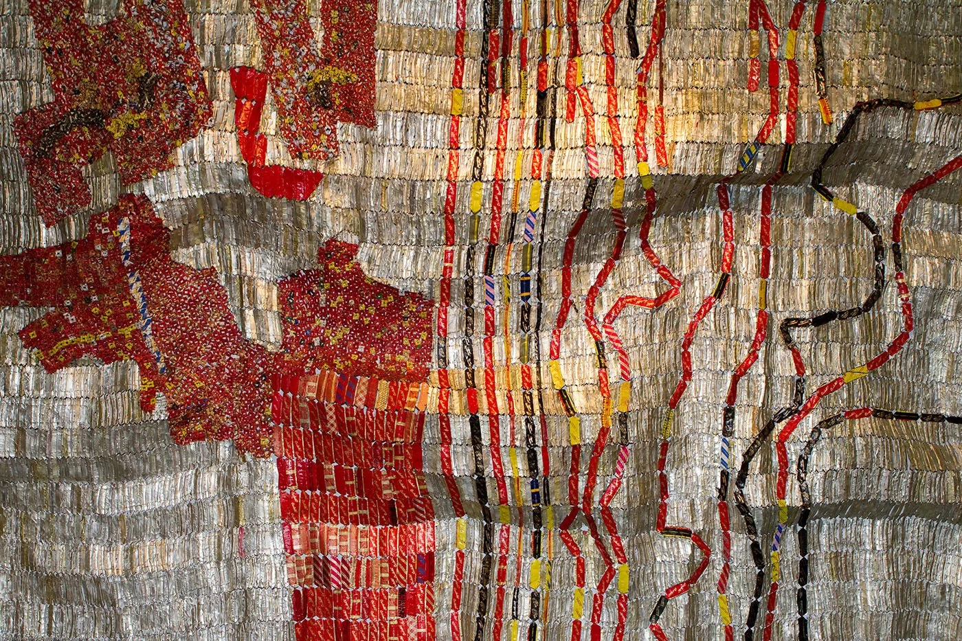 Detail of an El Anatsui tapestry in red and silver bottle-cap metal