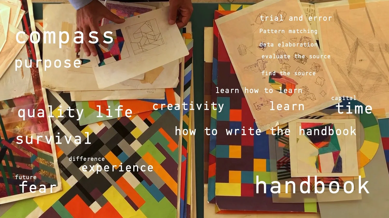 Hands holding a sheet of geometric drawings over a desk of colored paper cutouts
