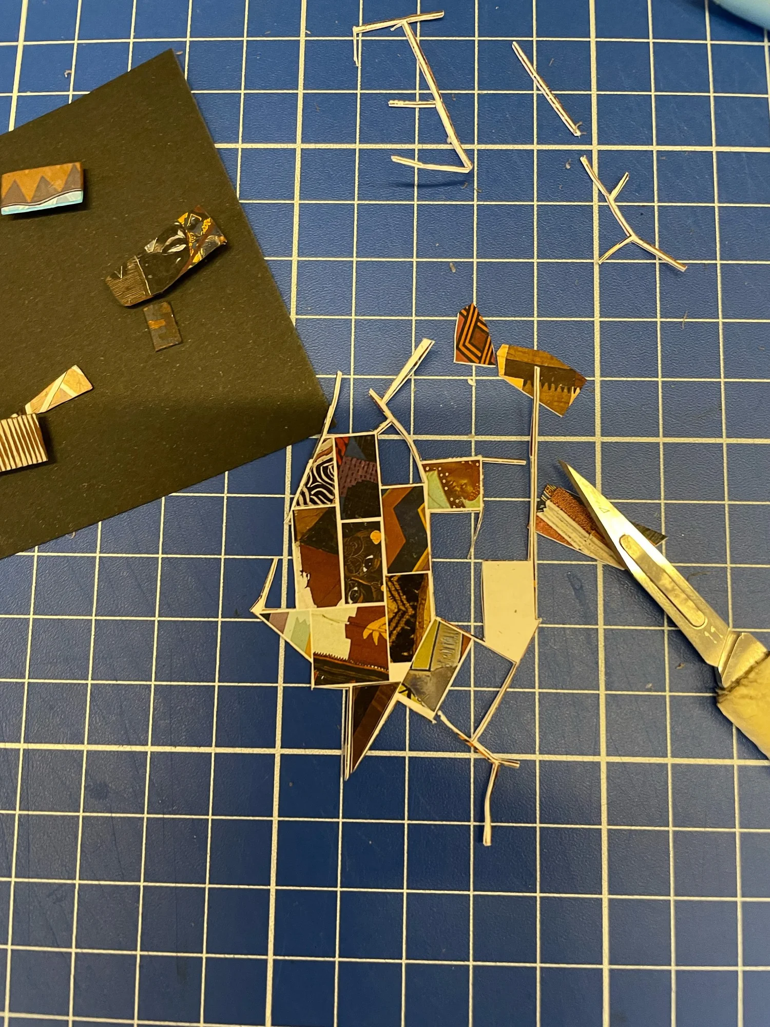 Cutting mat with a scalpel, thin paper strips and small patterned scraps, a hand-cut tile being assembled for a paper mosaic
