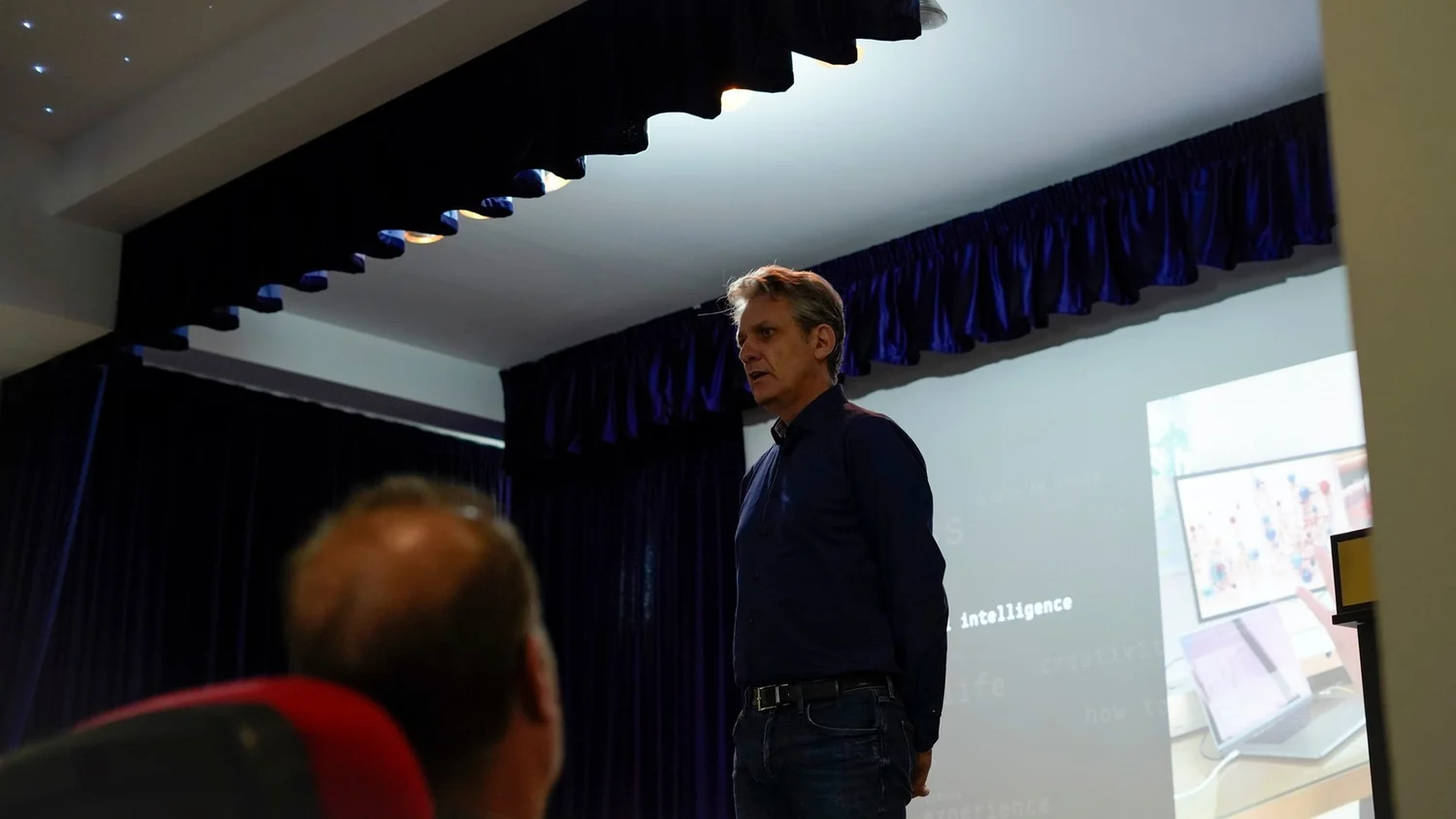 Charis Tsevis speaking in front of a projected slide with the word intelligence