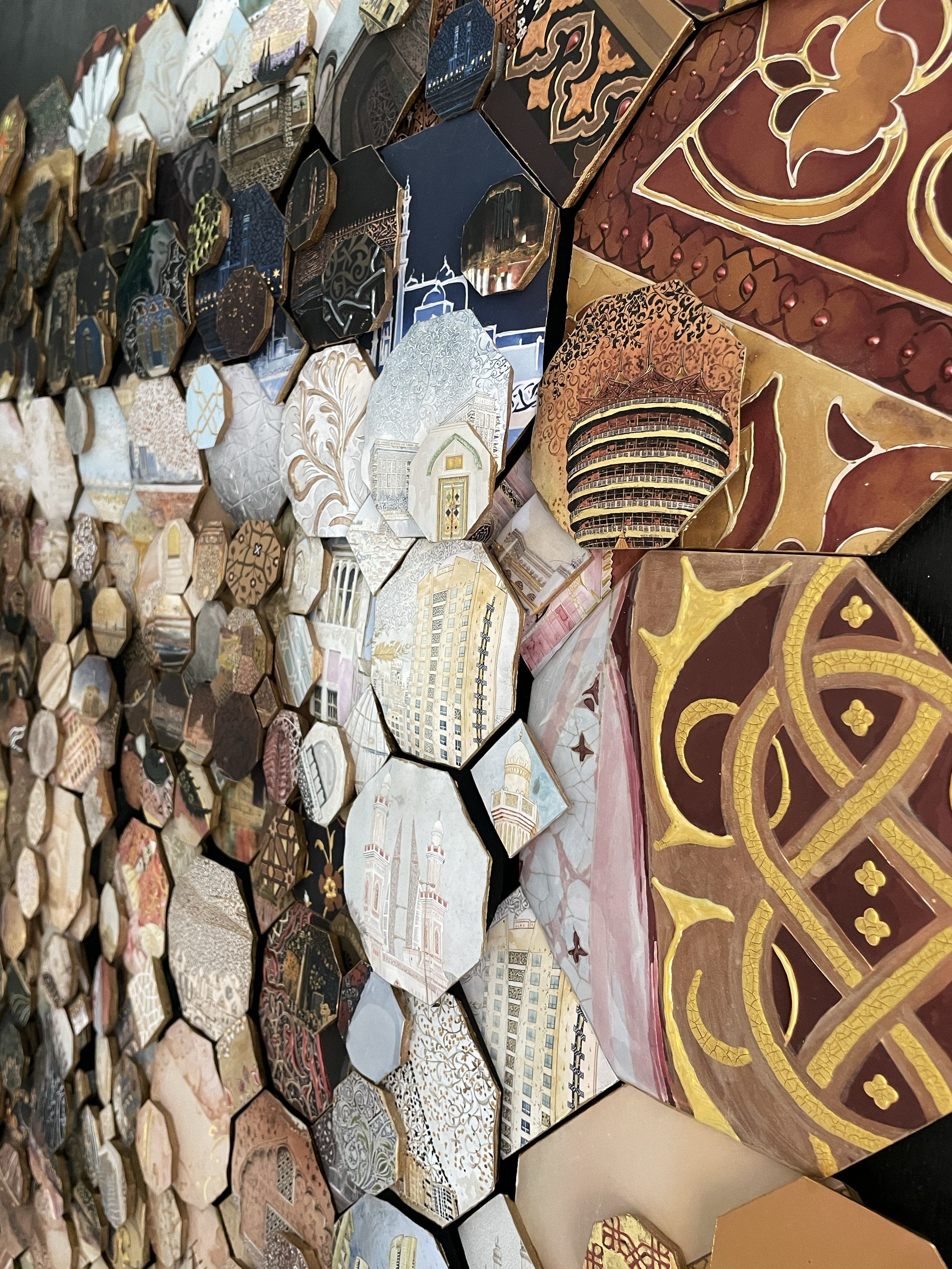 Side view of a mosaic wall of small octagonal tiles with towers, buildings and gold patterns, a large knotwork tile at right