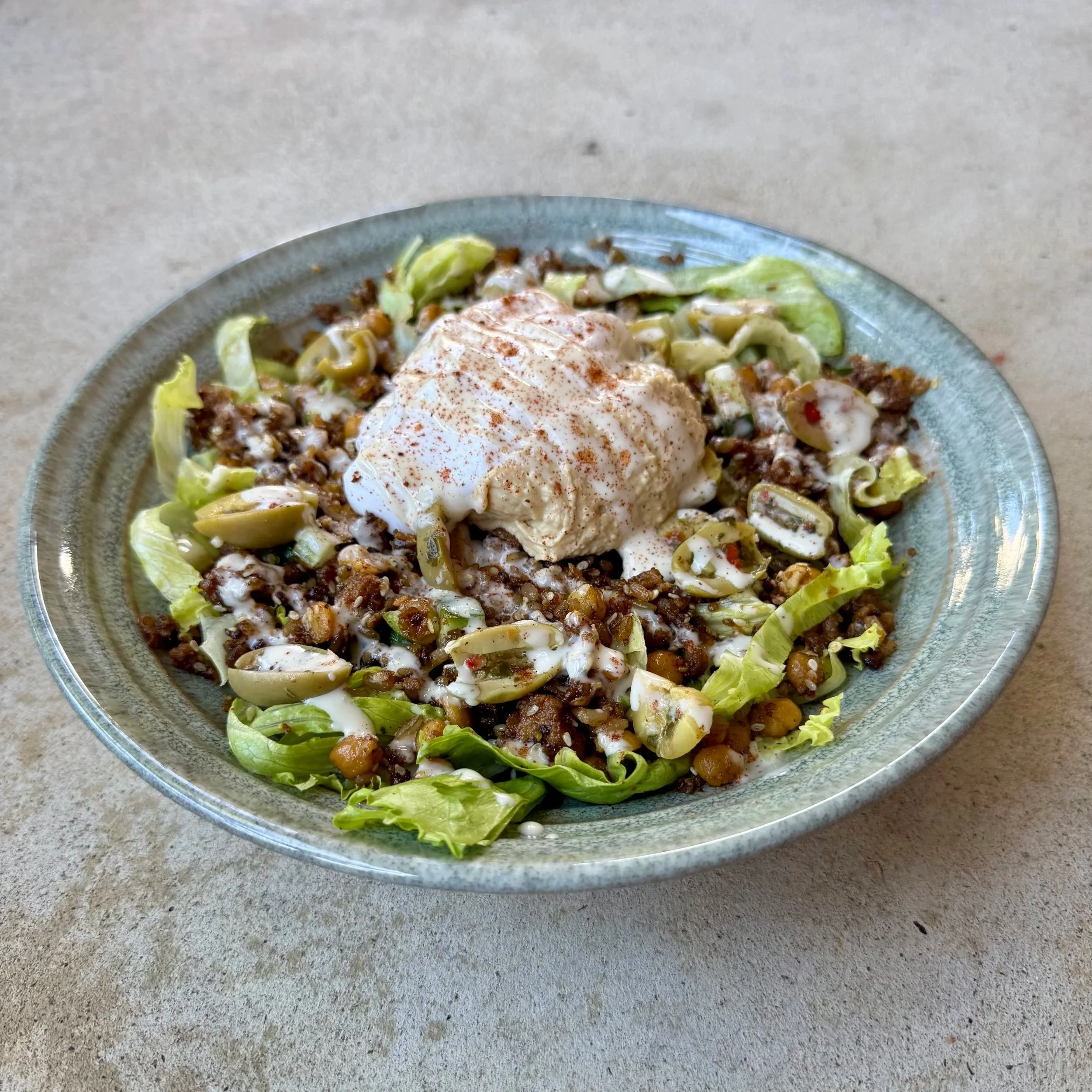 Bowl of seasoned ground beef, shredded lettuce, diced tomatoes, sour cream, and a poached egg garnished with paprika on a ceramic plate.
