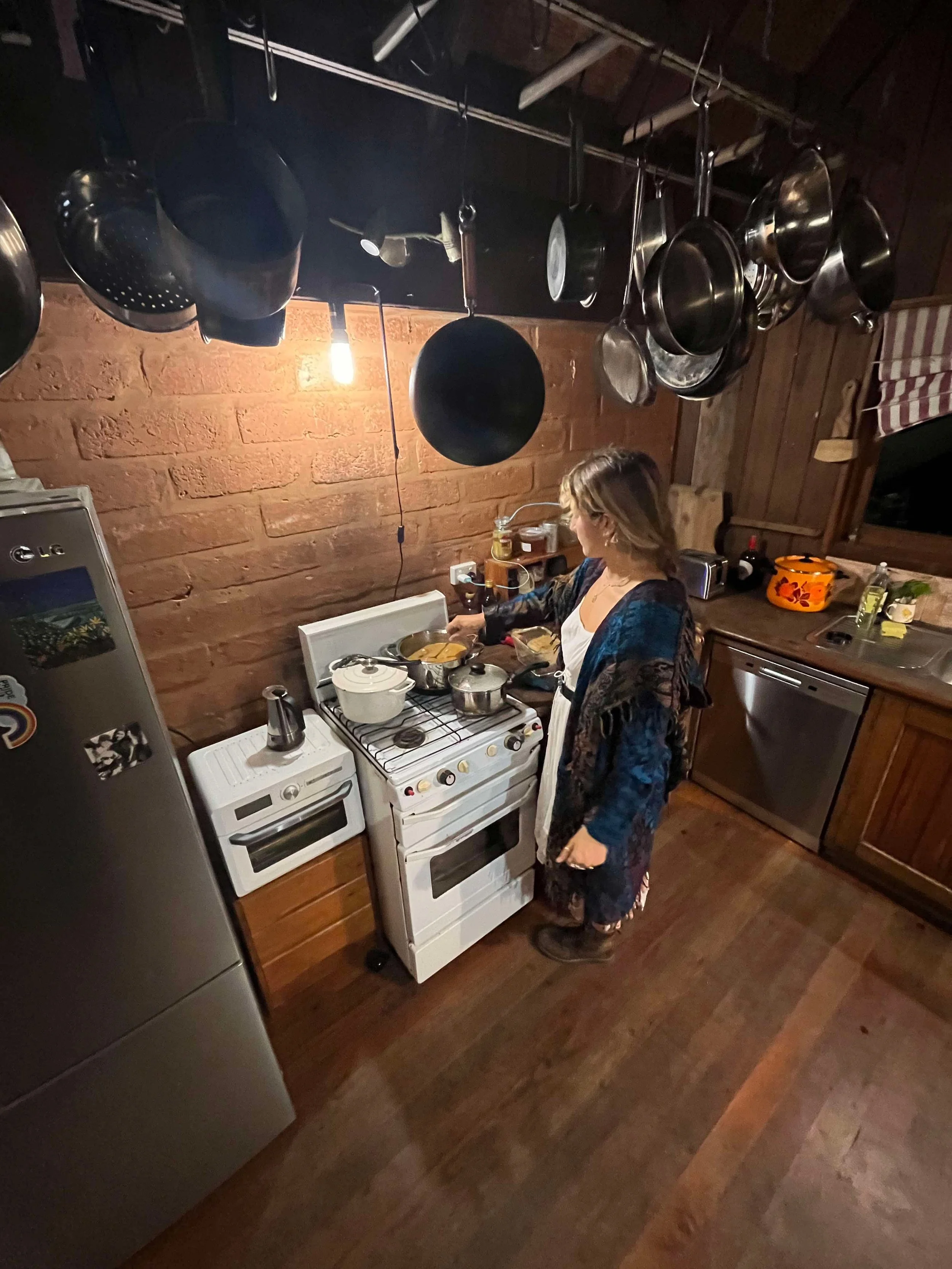 A woman cooking in a rustic kitchen with wooden walls and hanging pots and pans.