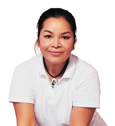 Eine Masseurin (Yanisa Borys) mit schwarzen Haaren, die ein weißes T-Shirt trägt, lächelt freundlich in die Kamera.