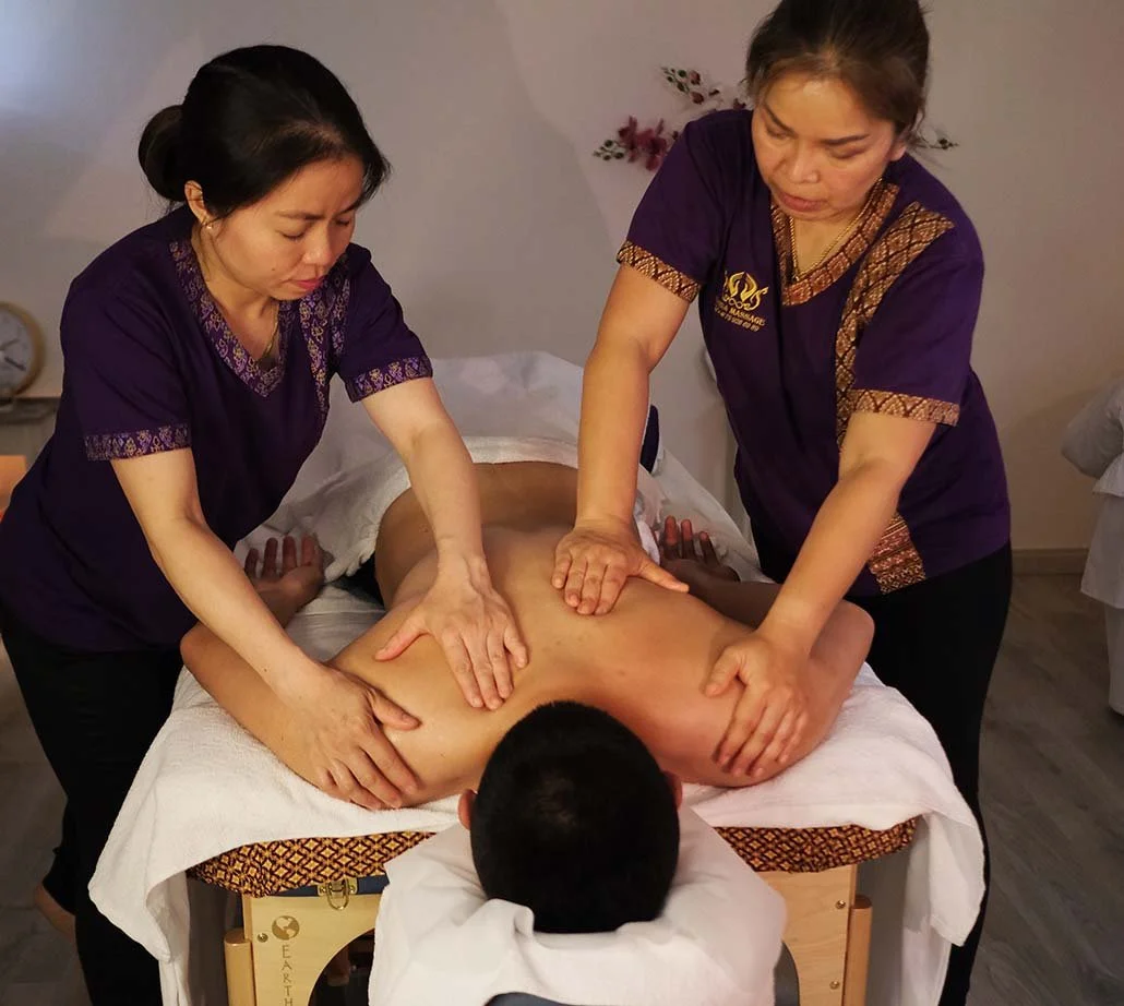 Zwei Frauen geben einem Mann eine Massage auf dem Bauch, während er auf einer Massagebank liegt.