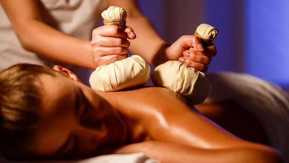 Durchführung einer Kräuterstempelmassage am Rücken einer Frau.