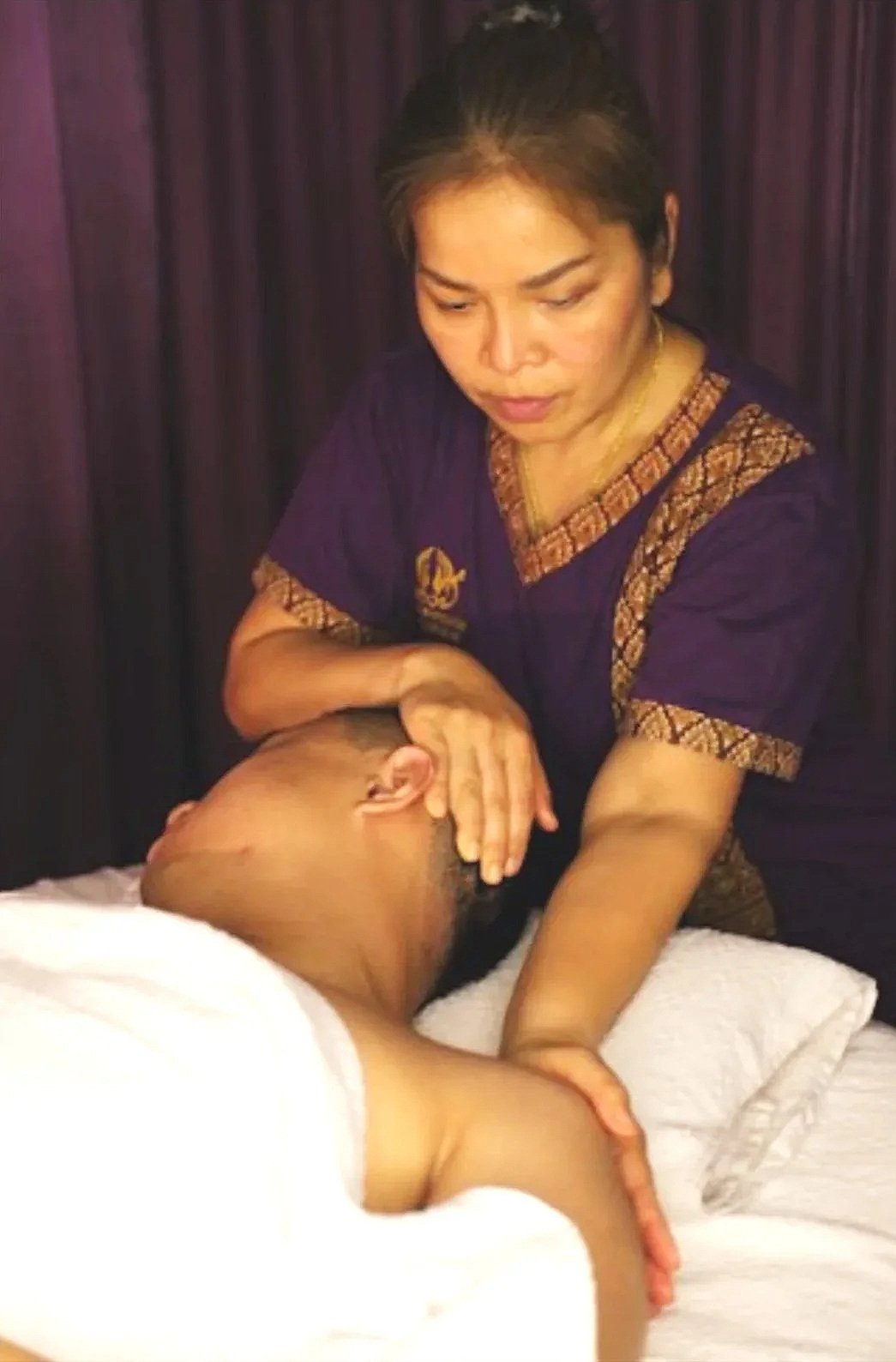 Die Masseurin Yanisa Borys führt eine Dehnungsmassage an einen Kunden mit einem violetten Vorhang im Hintergrund durch.