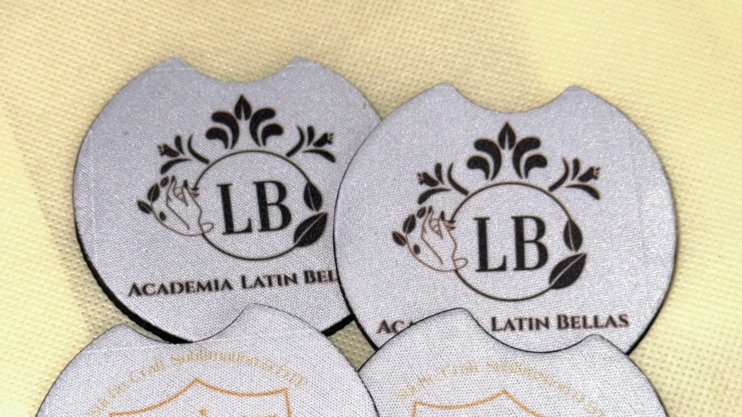Four circular embroidered patches, two with black and white design reading 'LB Academia Latin Bellas' and two with gold and white design reading 'GYC' with a shield and decorative elements.