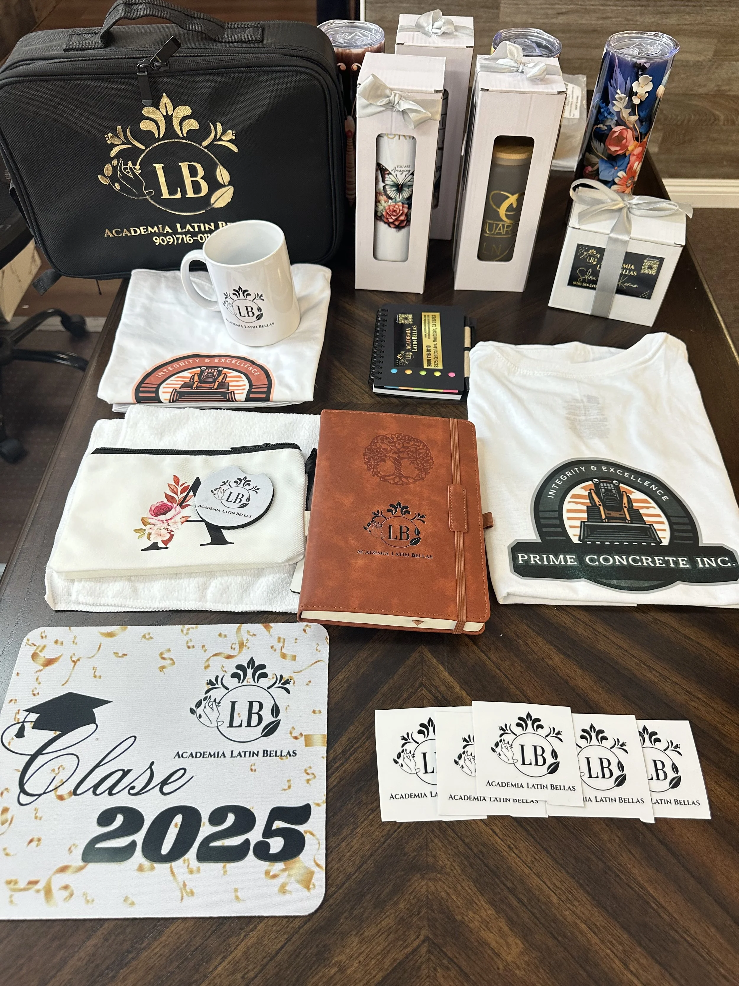 Graduation and school supplies from Academia Latin Bellas, including a black carrying case, personalized mug, notebooks, T-shirts, cards, water bottles, and a sign reading 'Class of 2025'.