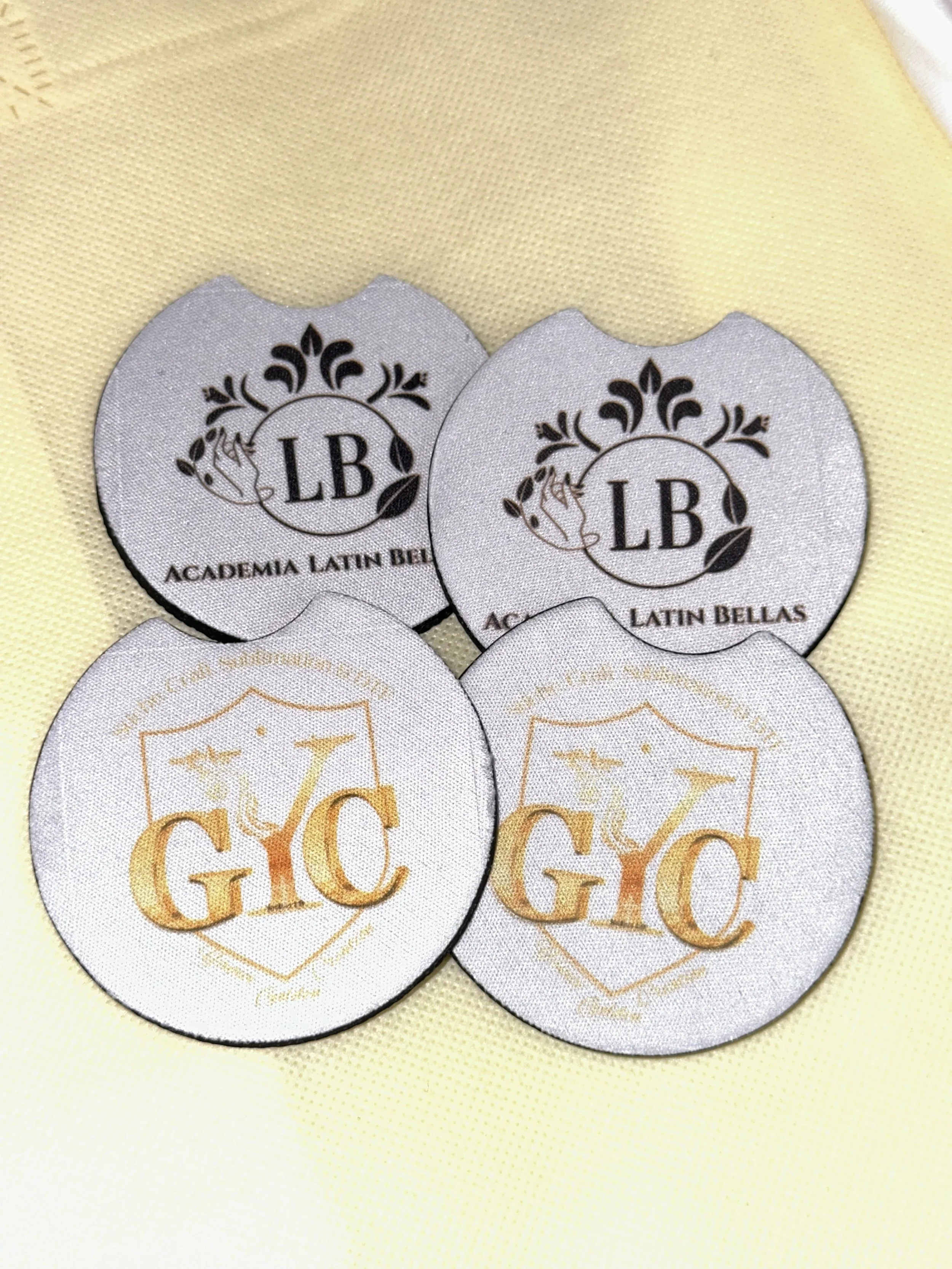 Four circular embroidered patches, two with black and white design reading 'LB Academia Latin Bellas' and two with gold and white design reading 'GYC' with a shield and decorative elements.