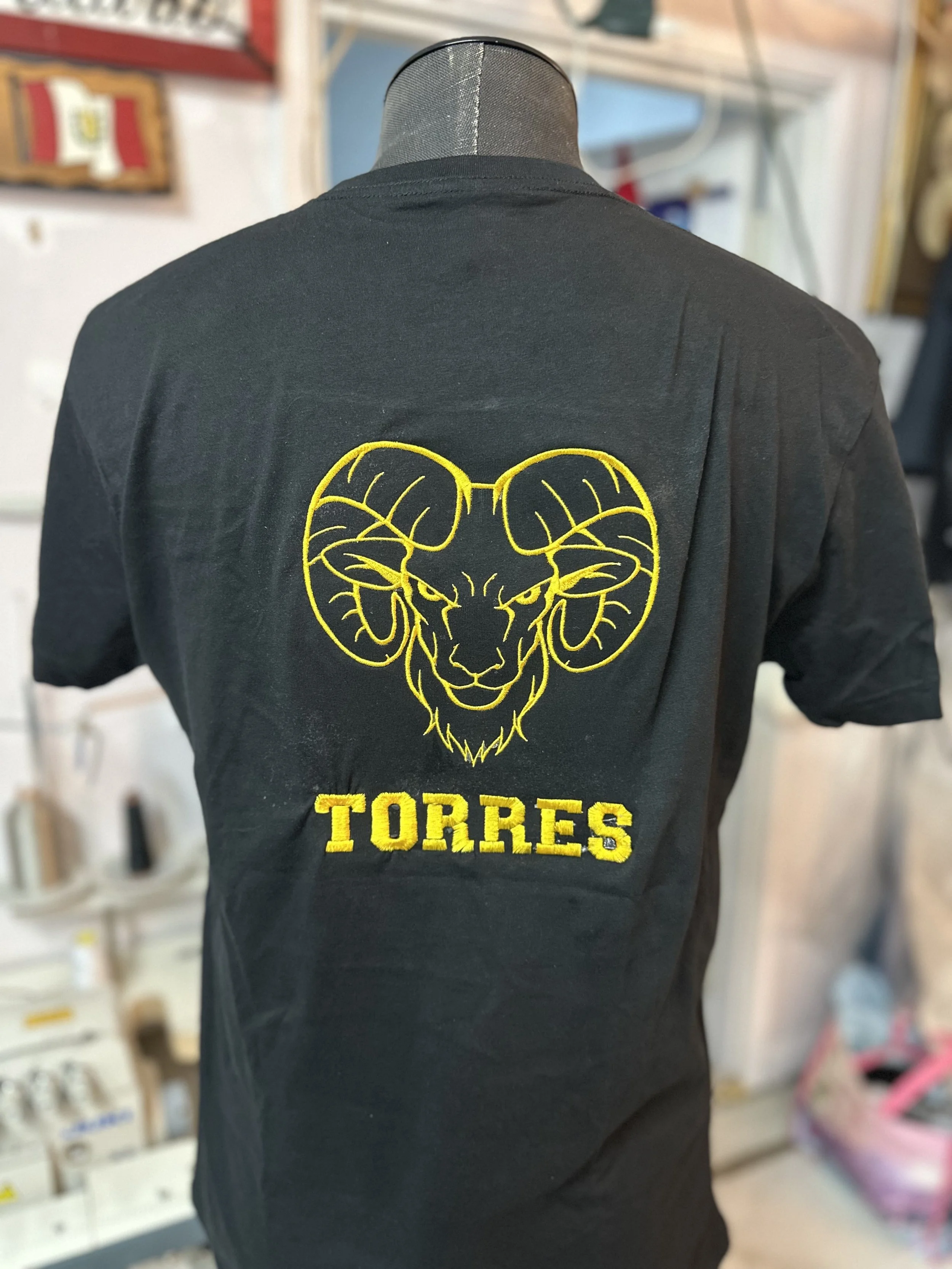 Back of a black t-shirt with a yellow embroidered design of a ram's head and the word "TORRES" below it.