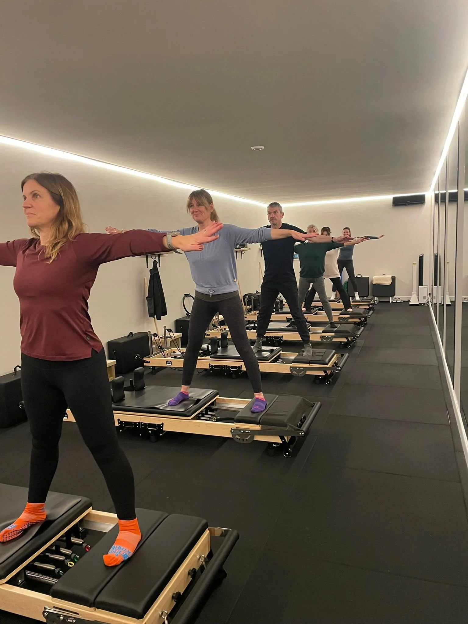 People participating in a Pilates or fitness class using reformer machines in a modern studio.