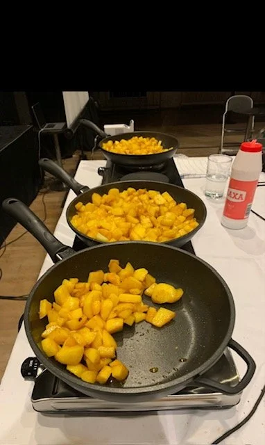 Three pans of cooking mangoes prepared during Vibrations of Blackness, transforming food preparation into a live ritual and communal gesture.