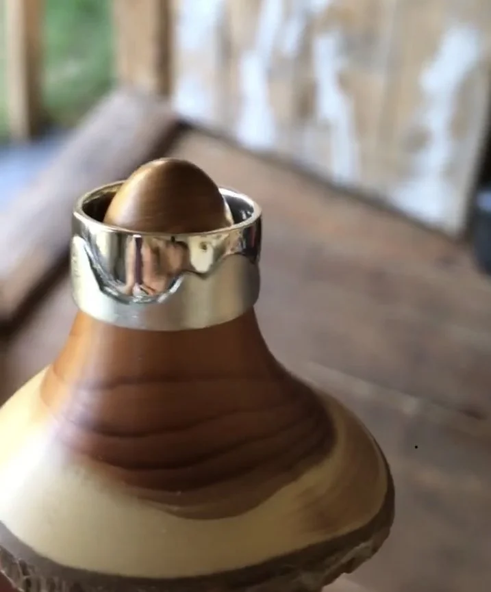A wooden massage tool with a rounded metal head, resting on a wooden surface inside a rustic setting.