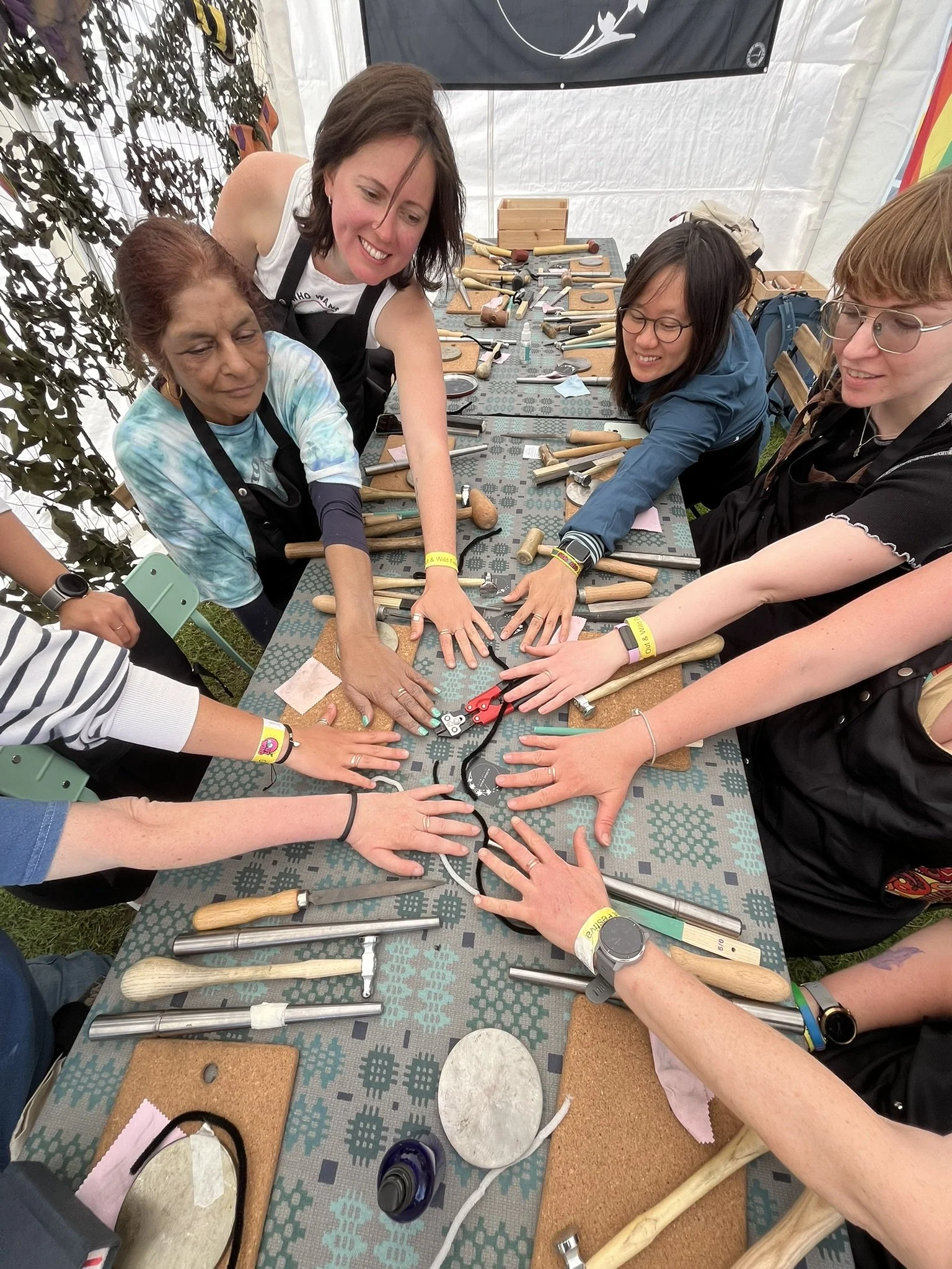 Group of people participating in a hands-on hammering activity at a workshop table inside a tent, with various tools and materials displayed.