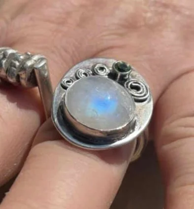 Close-up of a ring with a large, oval, opal gemstone and decorative metal detailing, worn on a finger.