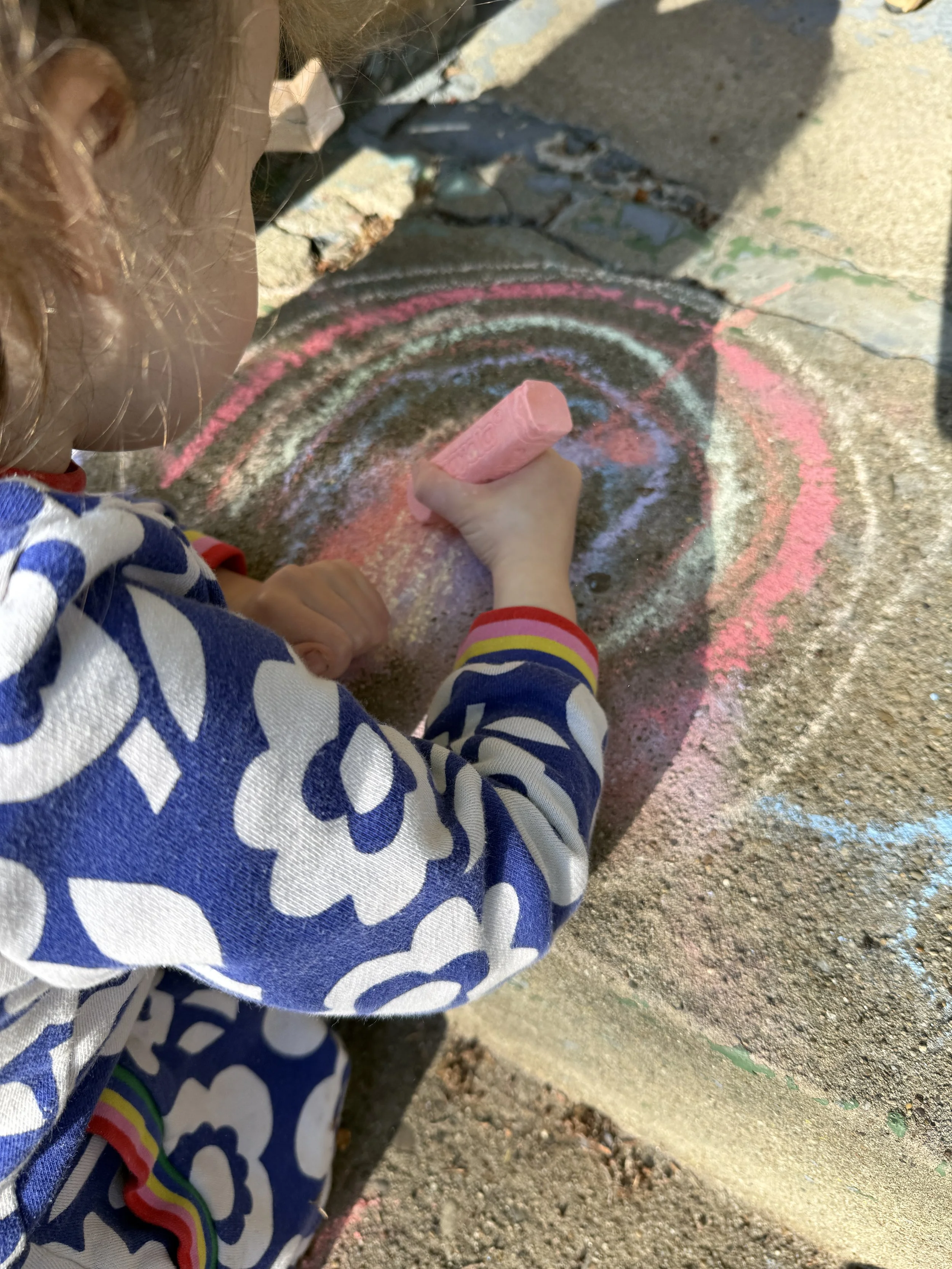 Child drawing colorful chalk circles on a sidewalk.