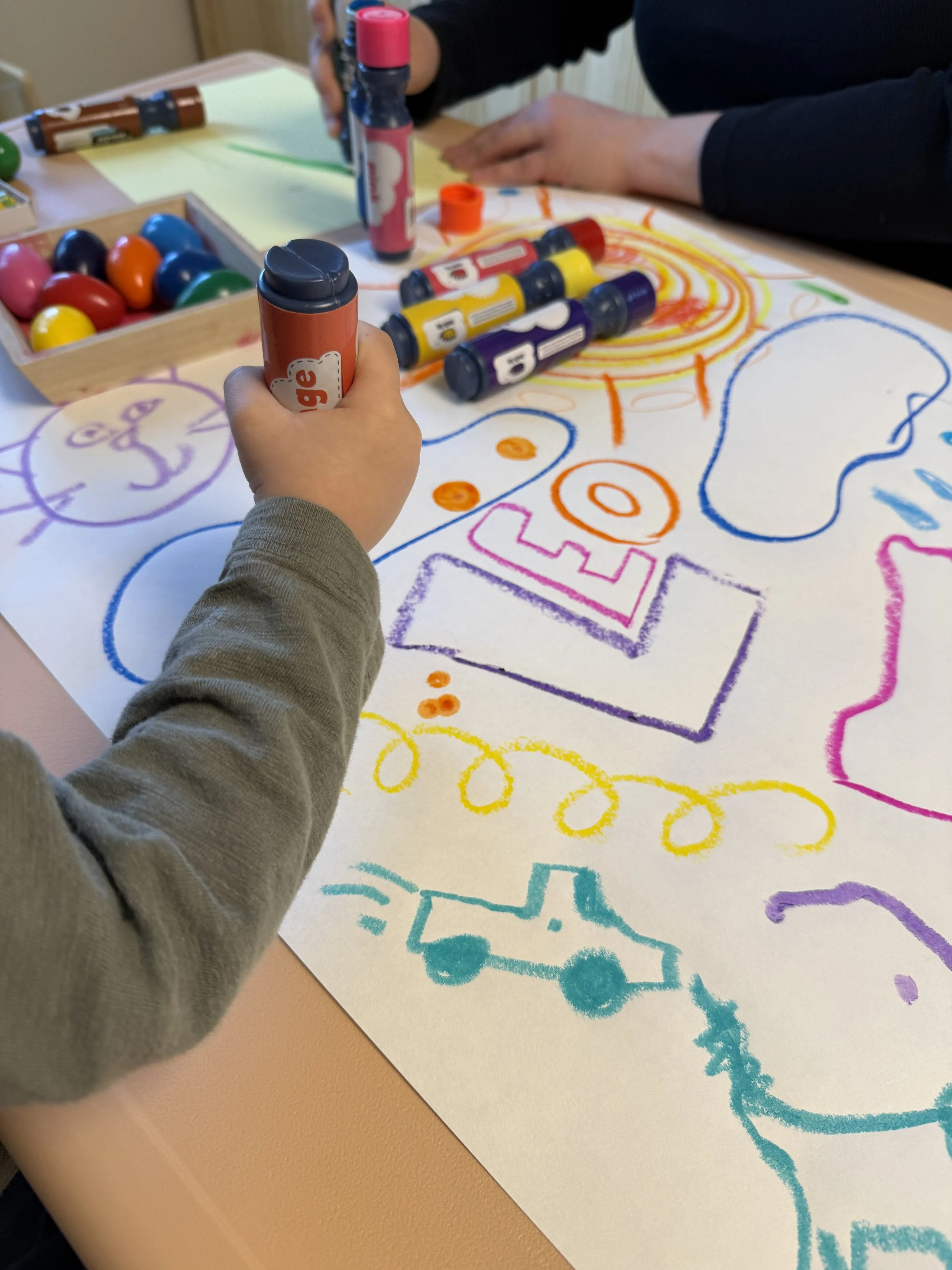 Child drawing on a large sheet of paper with colorful markers, creating various shapes and designs.
