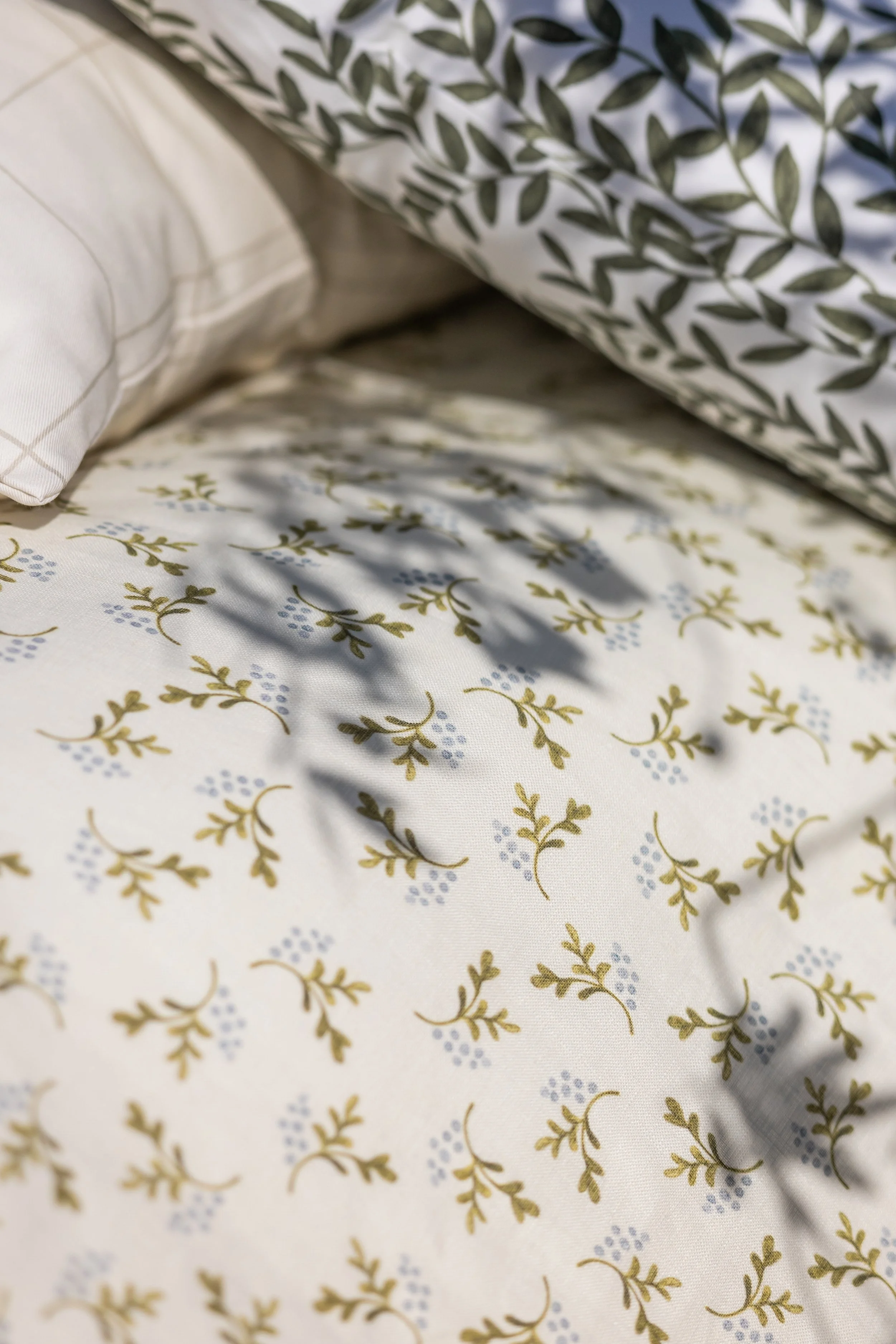 Close-up of a bed with floral-patterned sheets and pillows, featuring green and blue design elements on a white background.