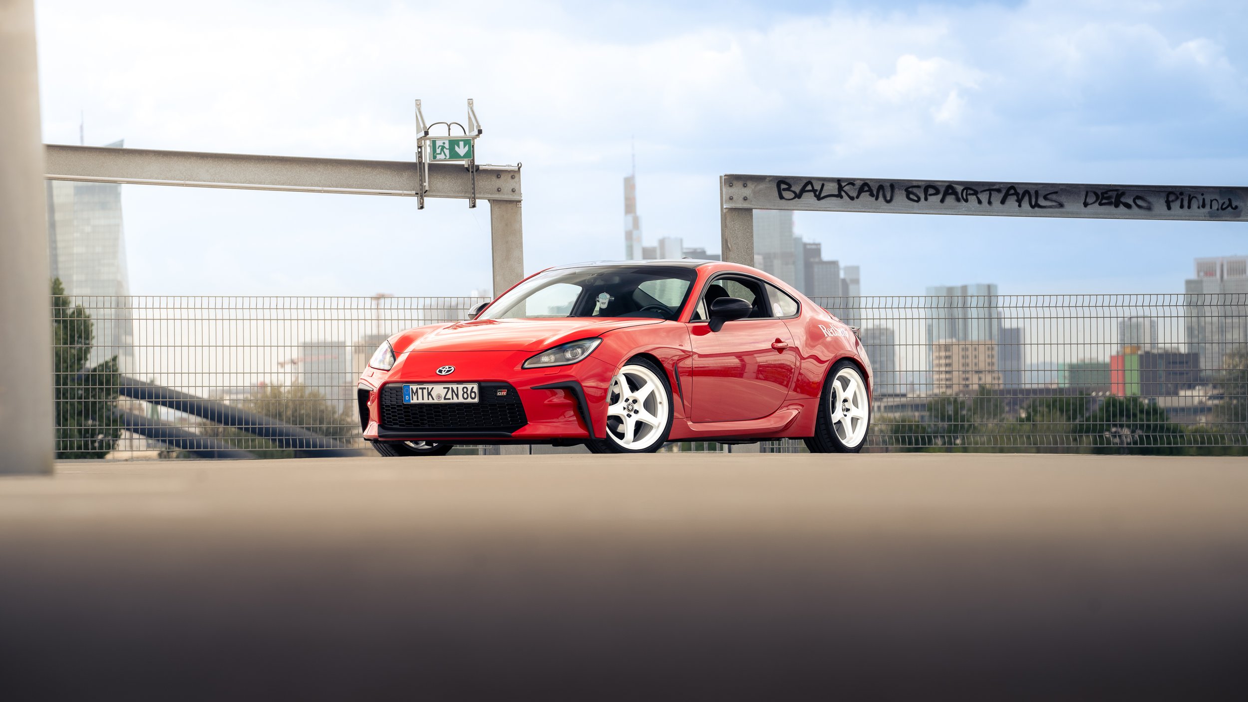 Roter Toyota GR86 auf einem Parkdeck mit Stadtblick im Hintergrund