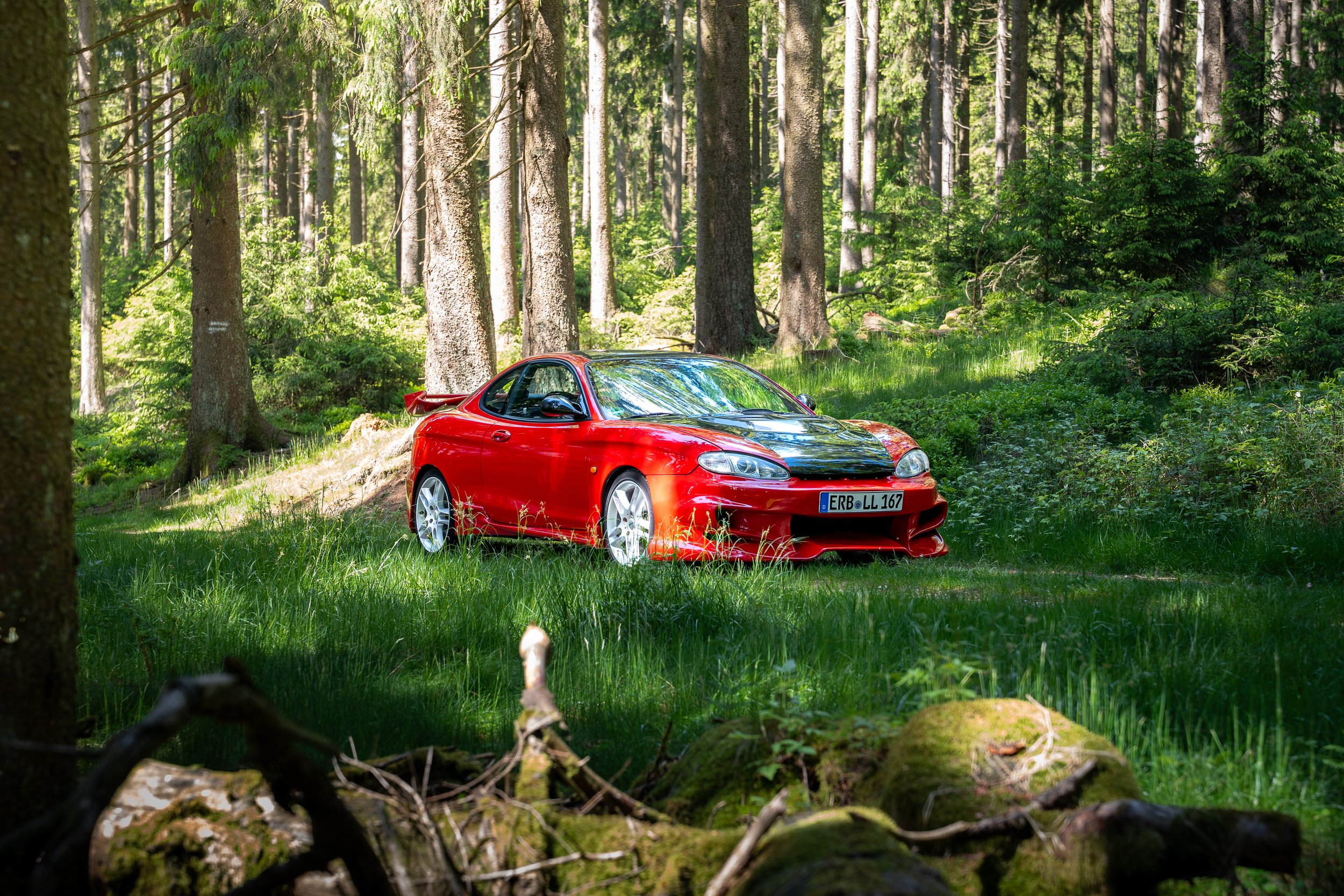 Roter Hyundai Coupé in einem grünen Wald