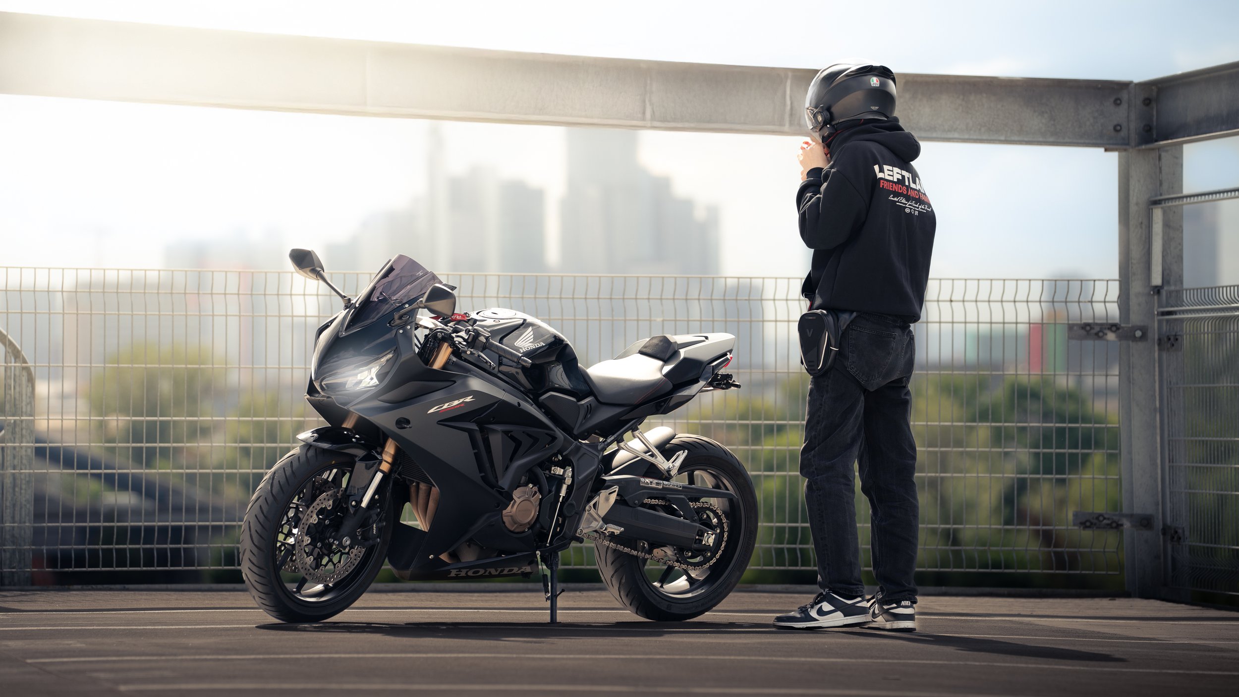 Person mit Helm steht neben schwarzer Honda CBR 650 R auf Parkplatz, im Hintergrund Skylineblick
