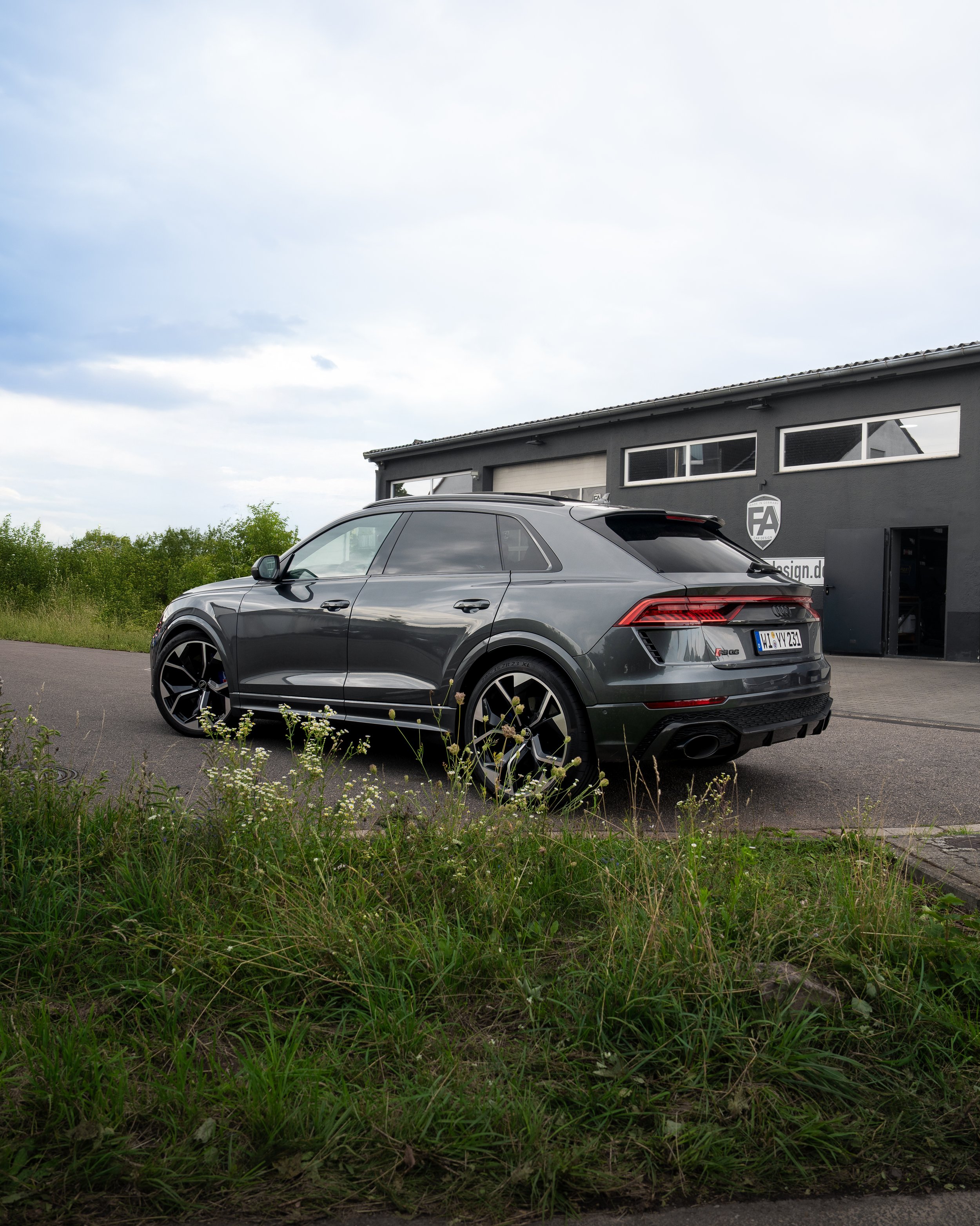 Ein grauer Audi RS Q8 vor einem schwarzen Gebäude, grüne Wiese mit Blumen im Vordergrund.