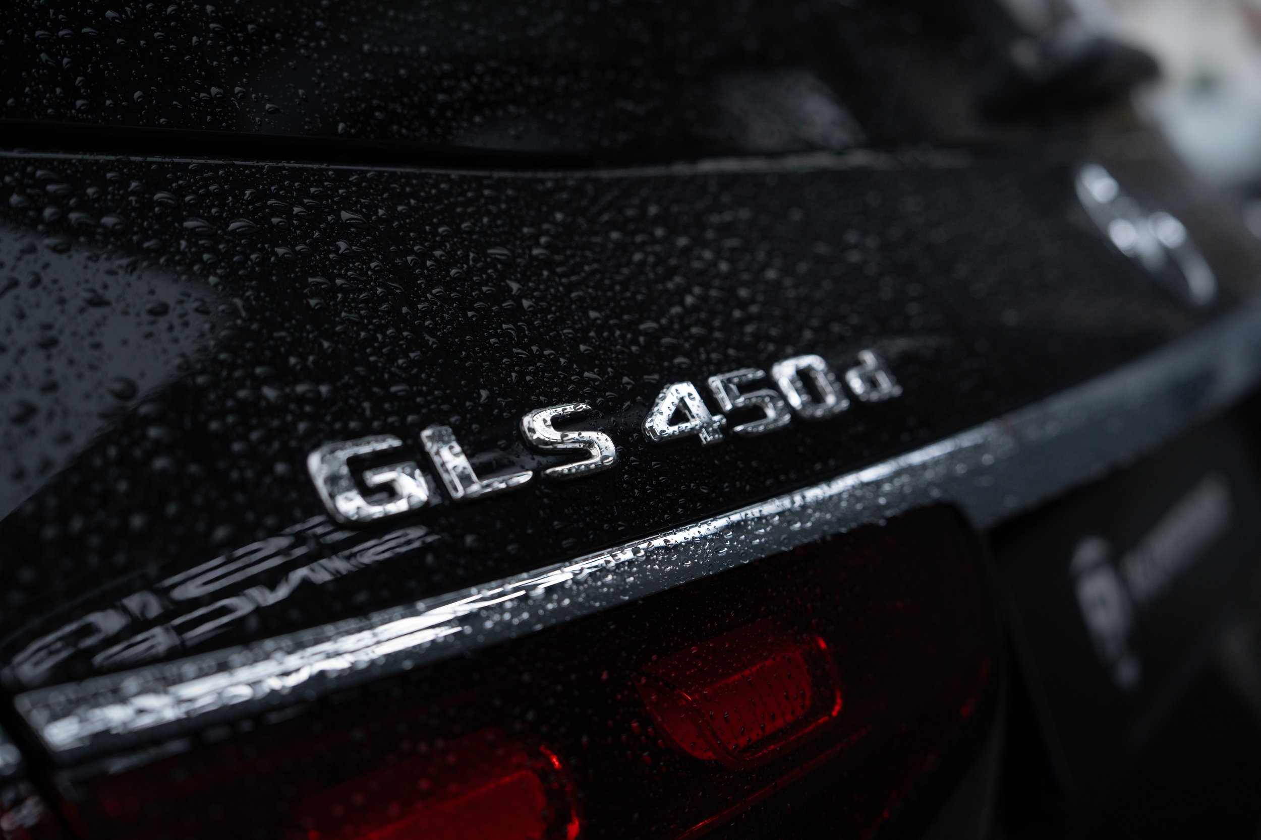 Nahaufnahme eines schwarzen Autos mit Regentropfen, das auf der Rückseite die Modellbezeichnung 'GLS 450d' trägt.