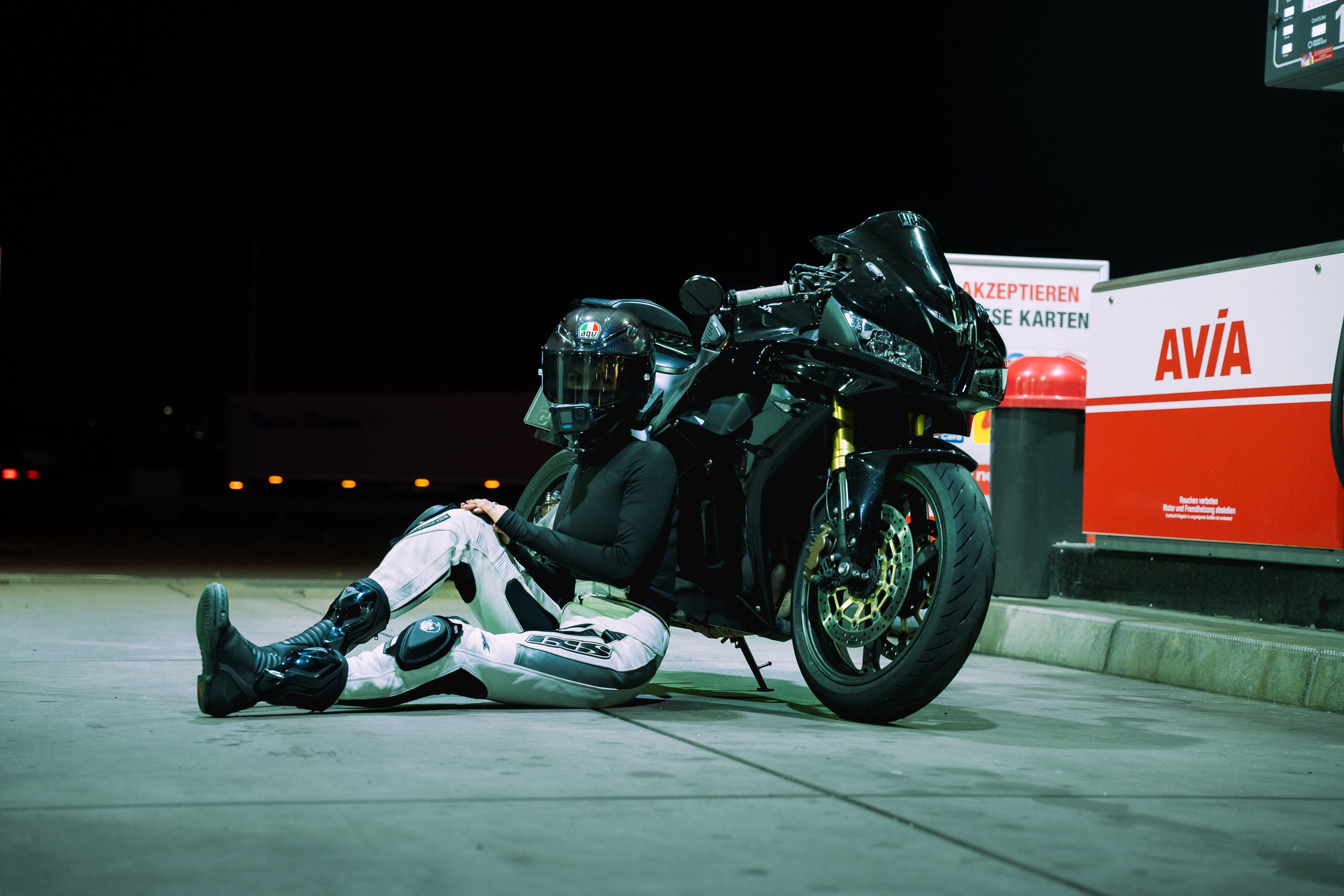 Motorradfahrer liegt auf dem Boden neben seinem schwarzen Motorrad in einer Tankstelle bei Nacht