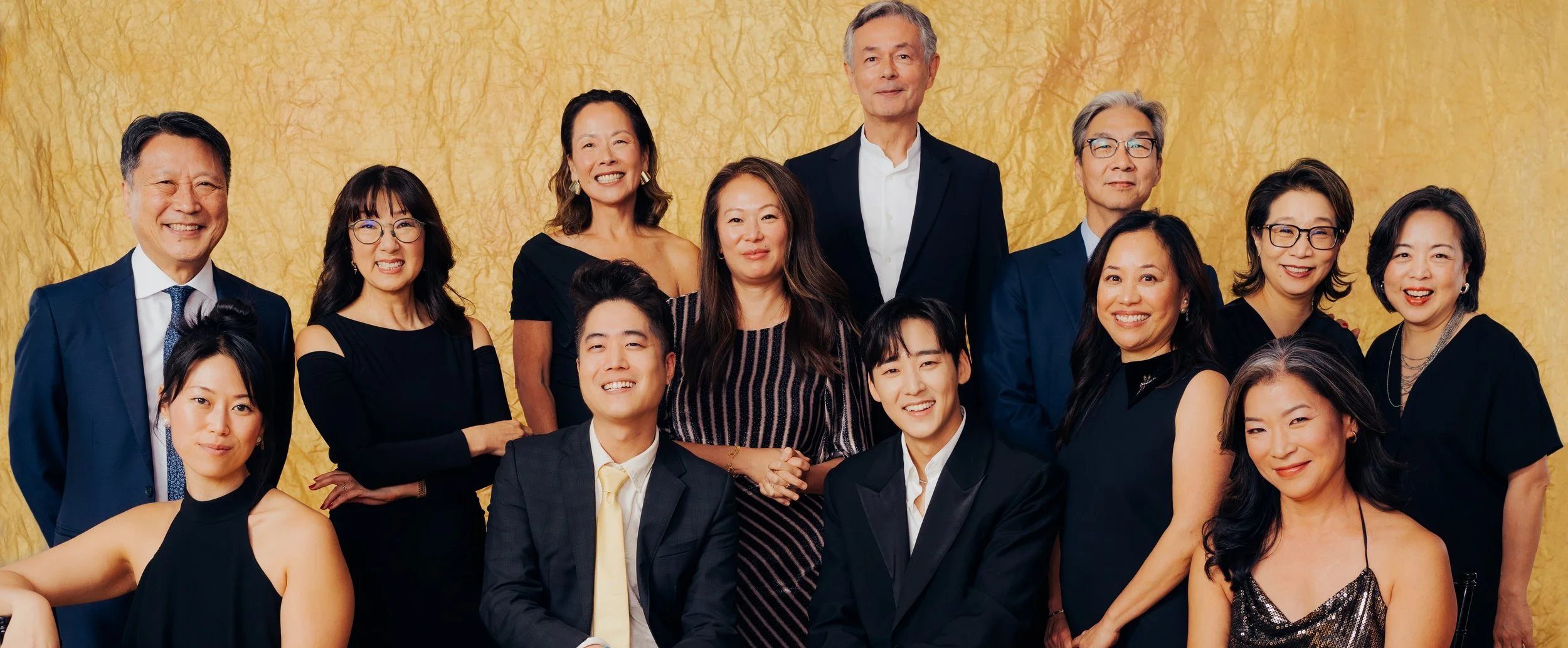 Group portrait of diverse adults in formal attire against a yellow textured background.